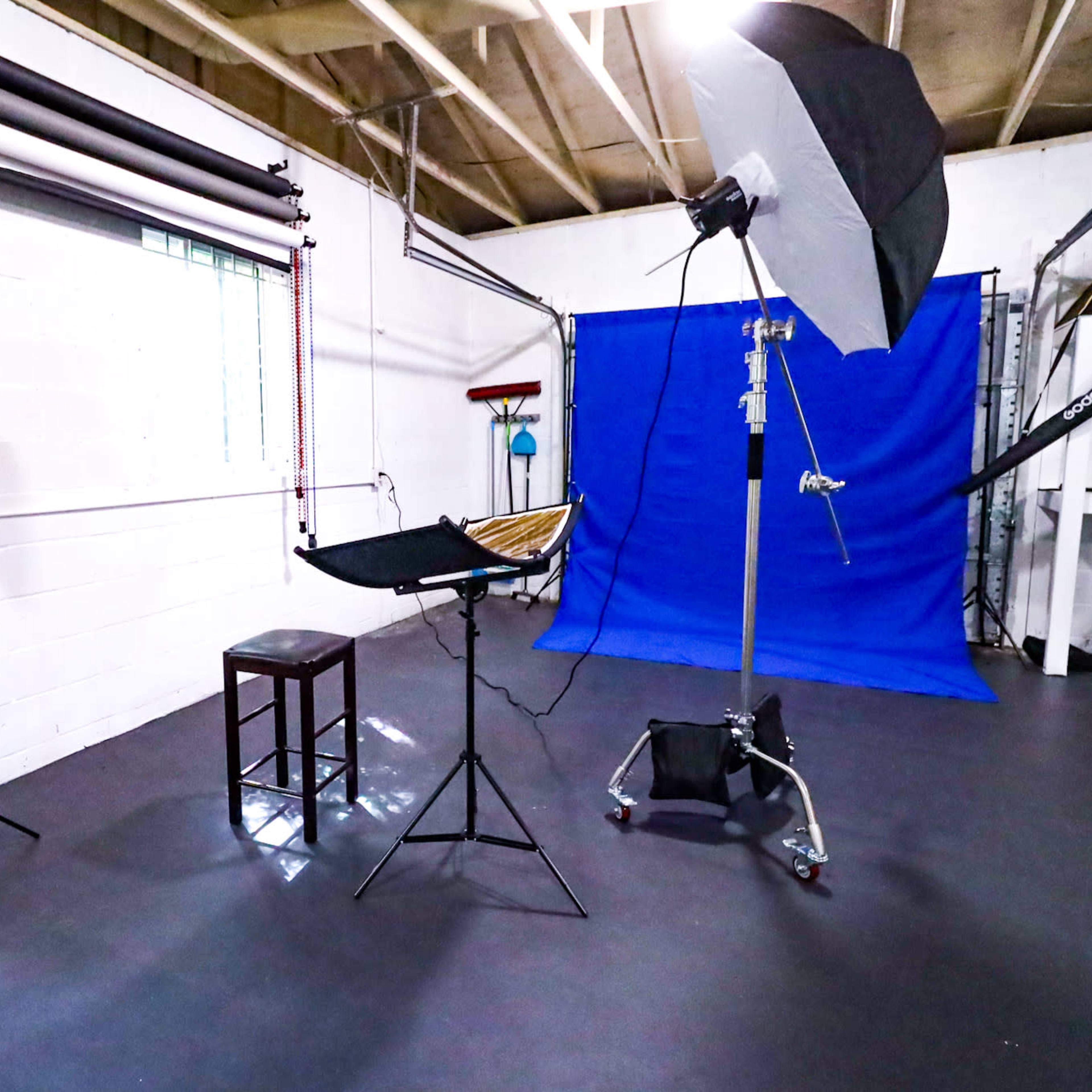 A photography studio with lighting equipment, a stool, and a blue backdrop.