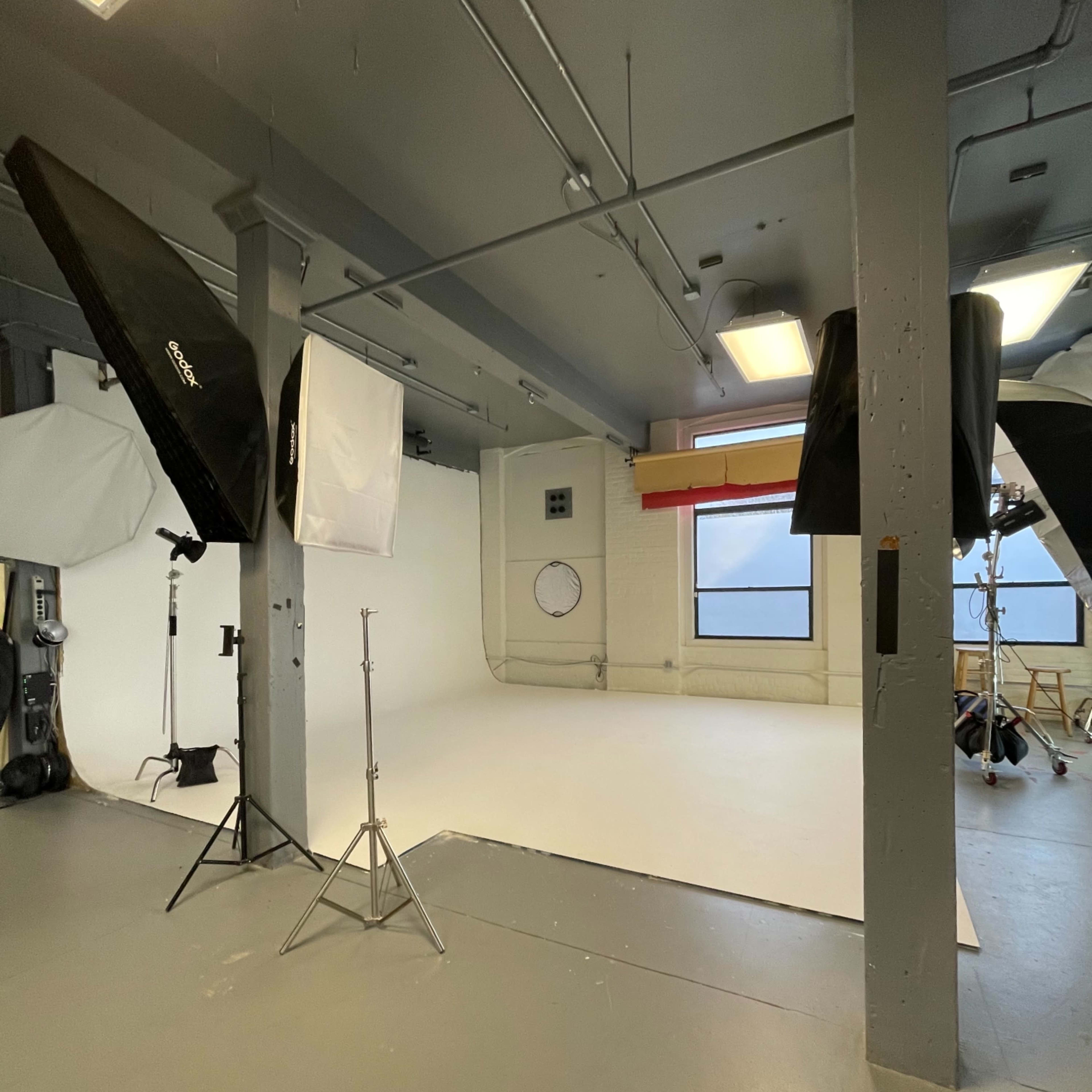 A photography studio with softbox lights and a white backdrop set up for a photoshoot.