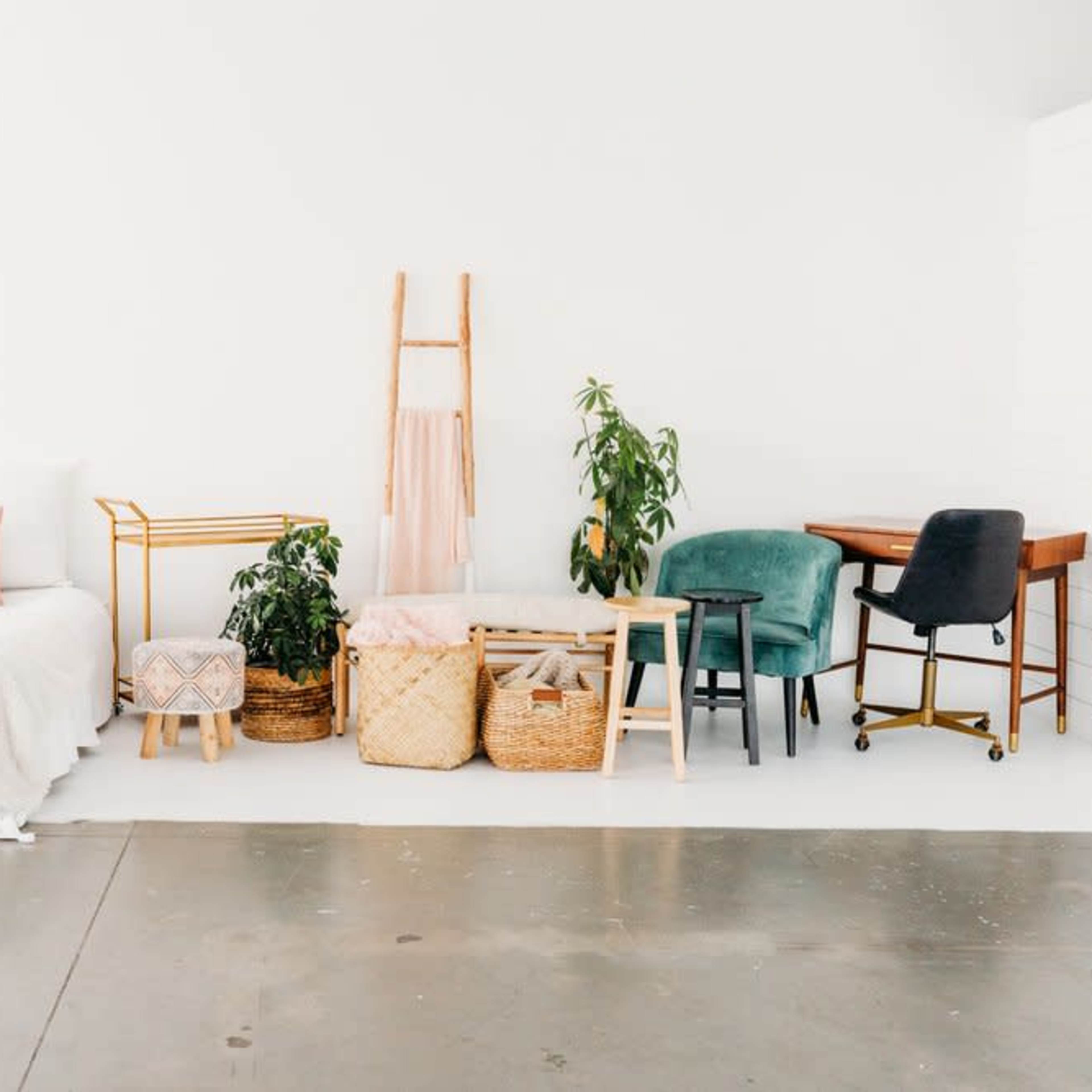 A minimalist room featuring a bed with white linens, various seating options, and plants displayed in woven baskets.