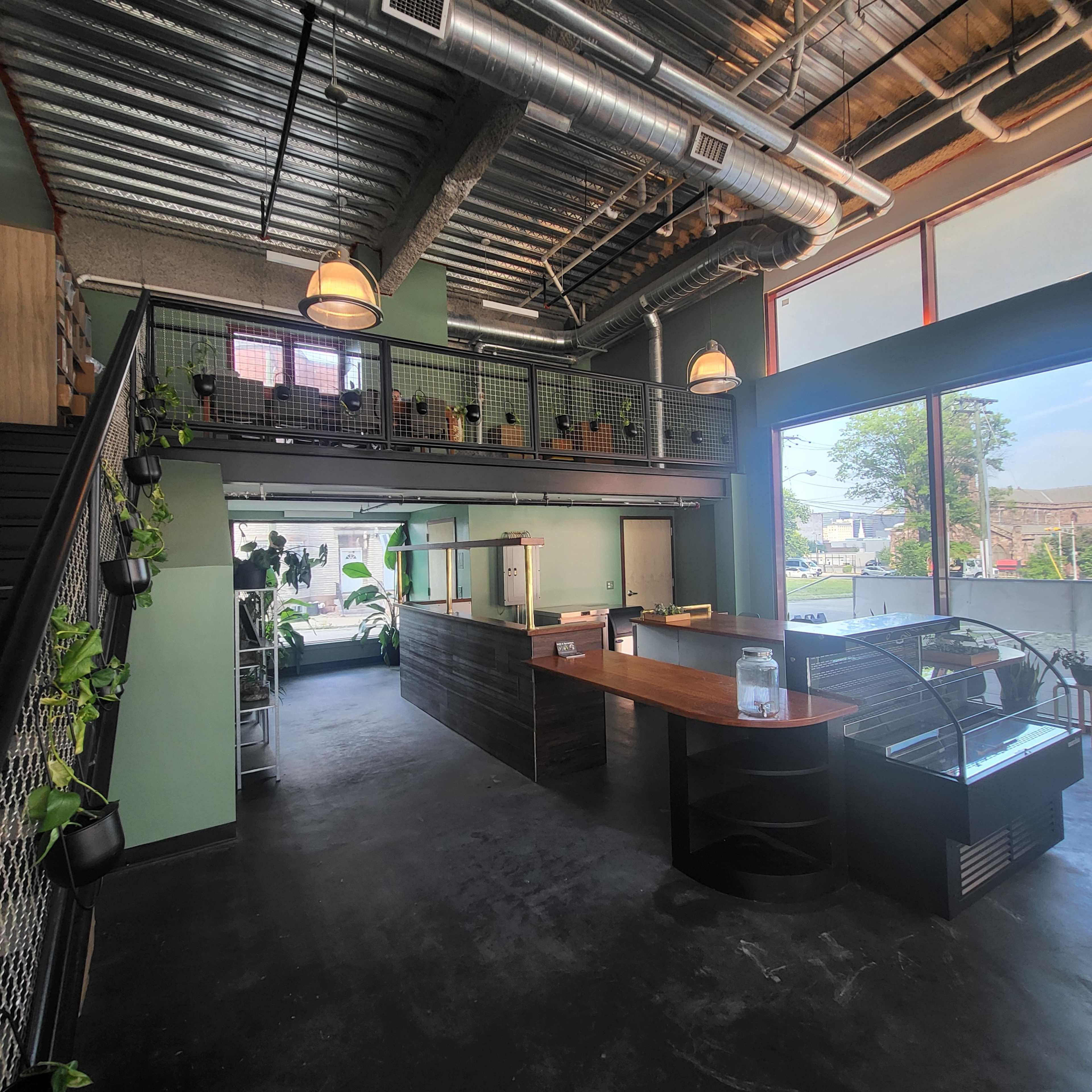 A modern interior of a cafe featuring a multi-level layout with a counter, seating area, and greenery.