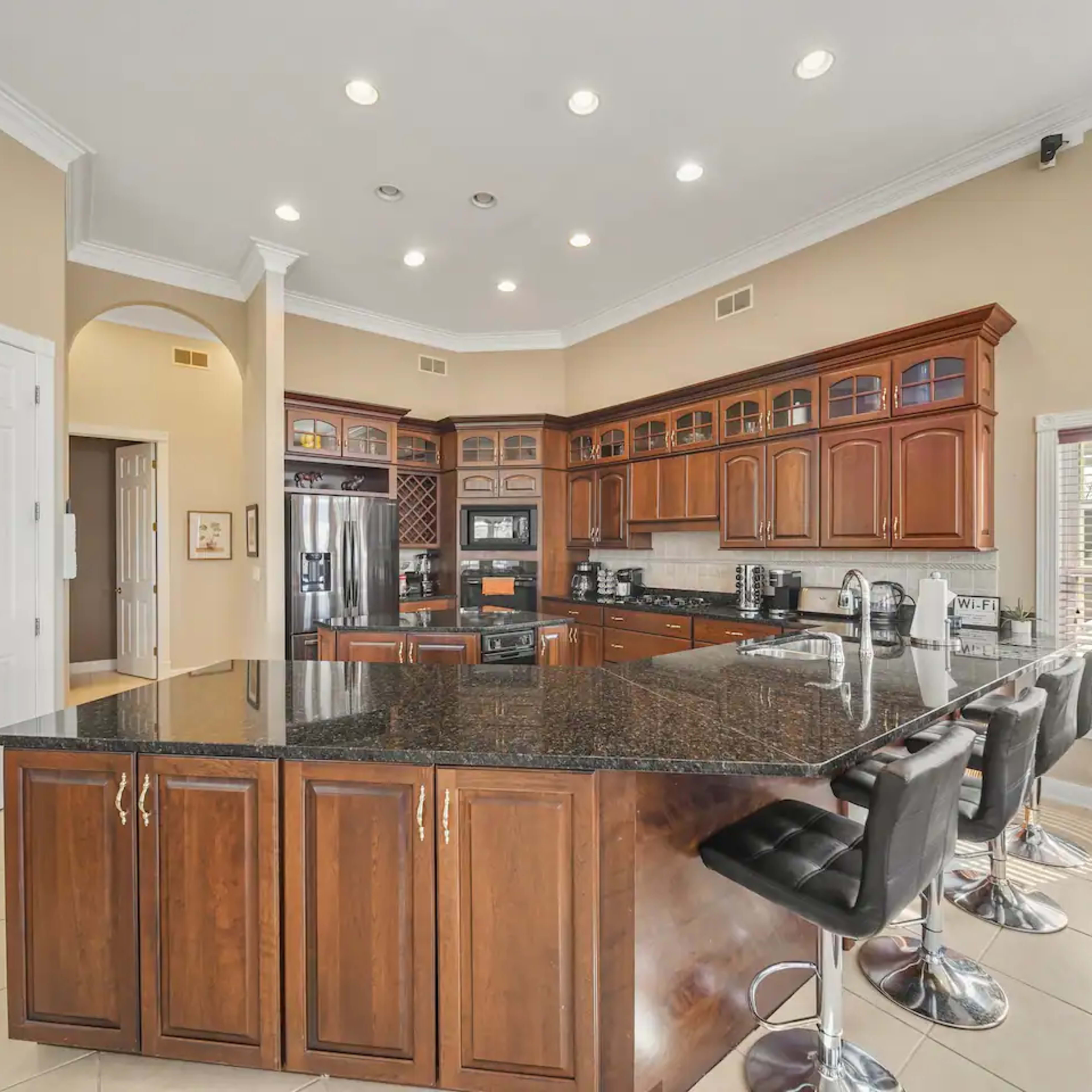 A modern kitchen featuring dark wood cabinets, a large granite island with bar stools, and stainless steel appliances.