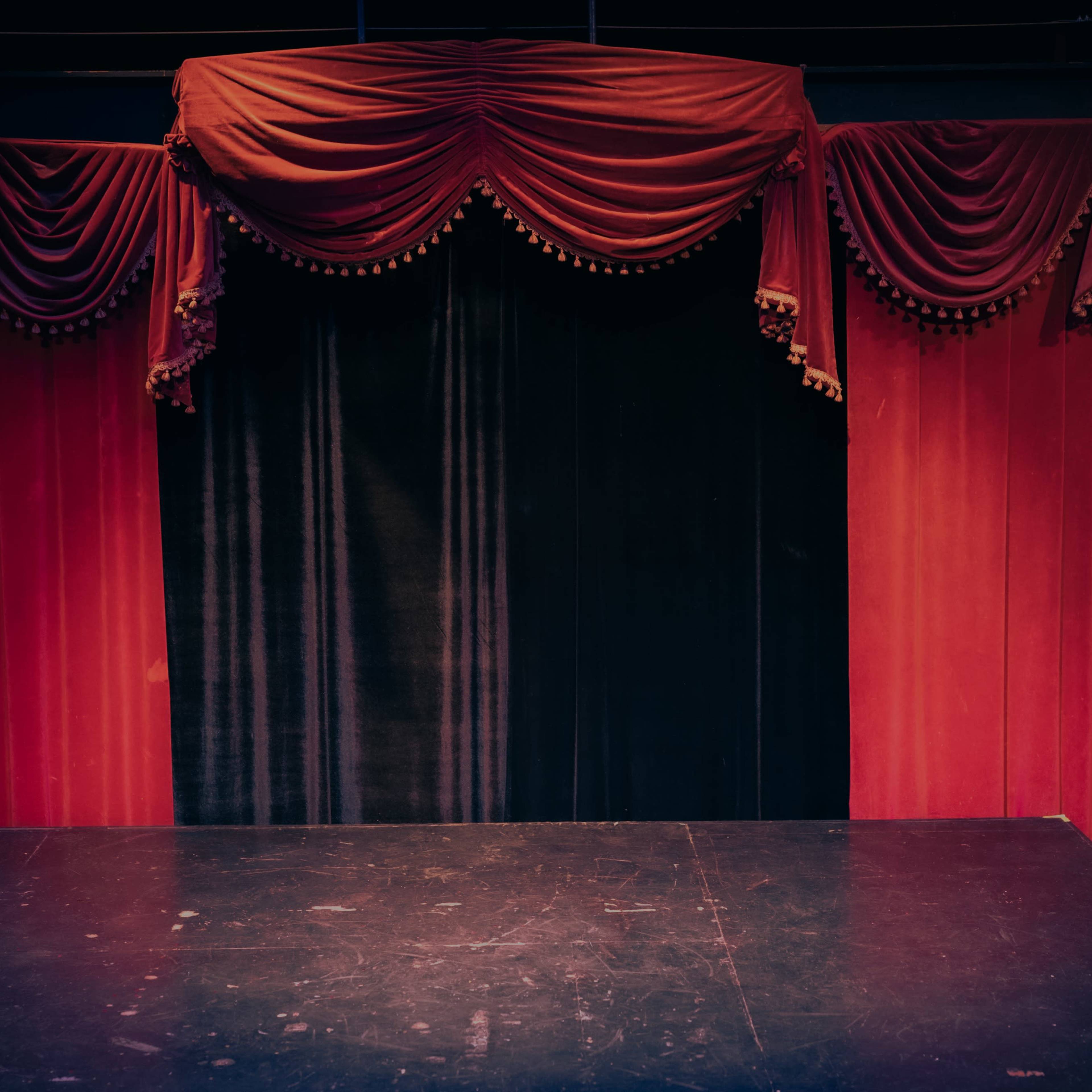 A stage with a red and black curtain draped above a dark floor.