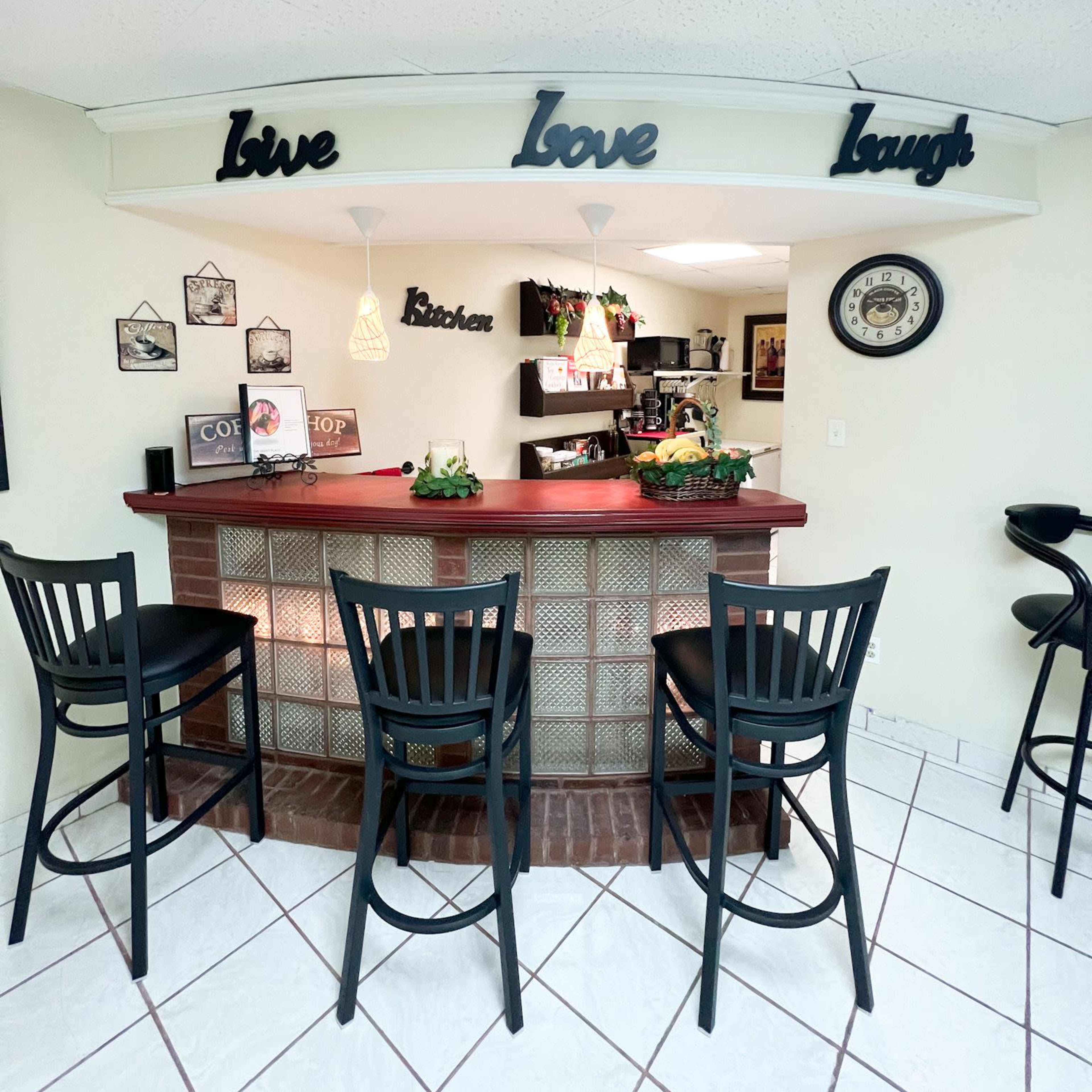 A small kitchen bar area features a red countertop with black stools and decorative signs reading "Love Love Laugh" above it.