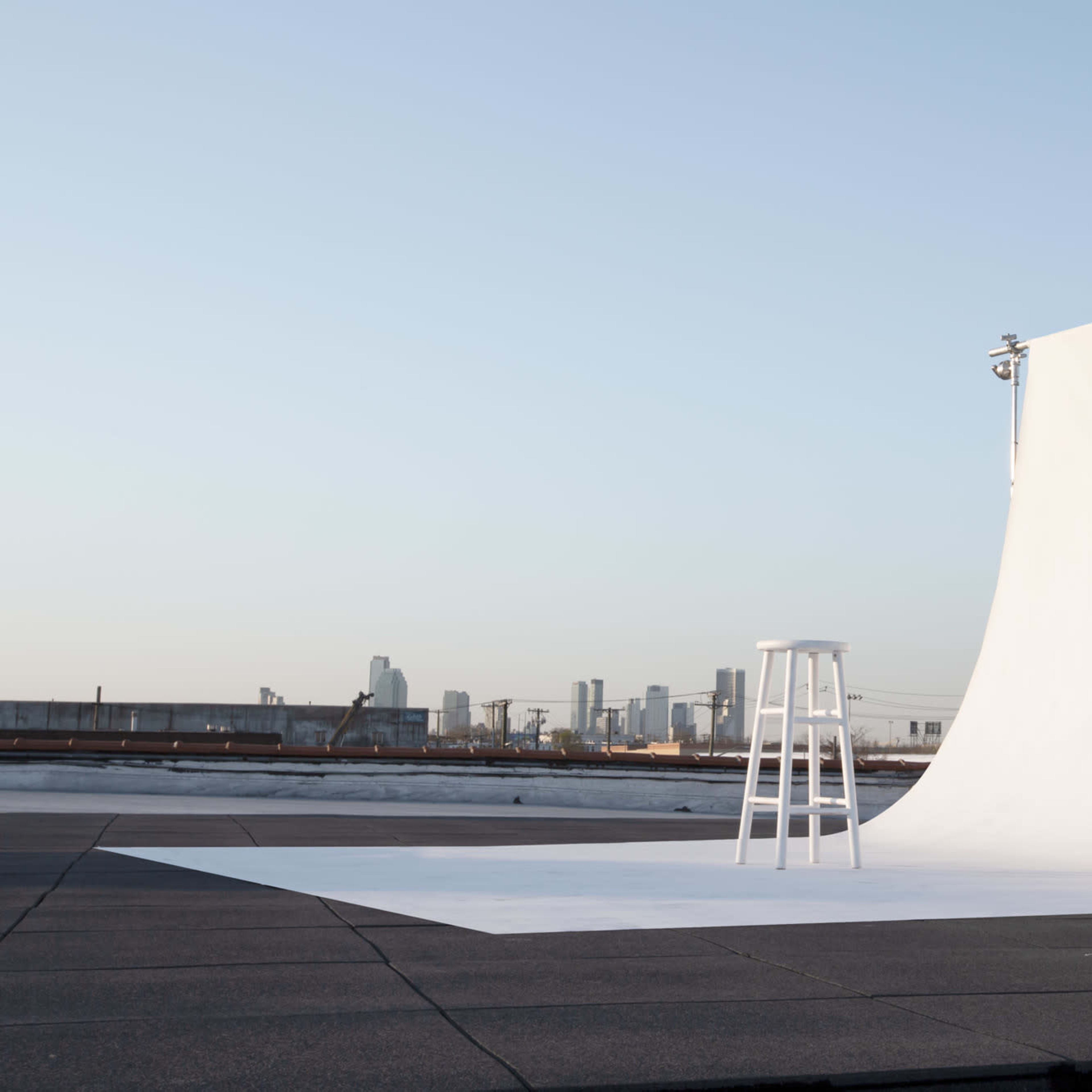 A white backdrop and stool are set up on a rooftop with a city skyline in the distance.