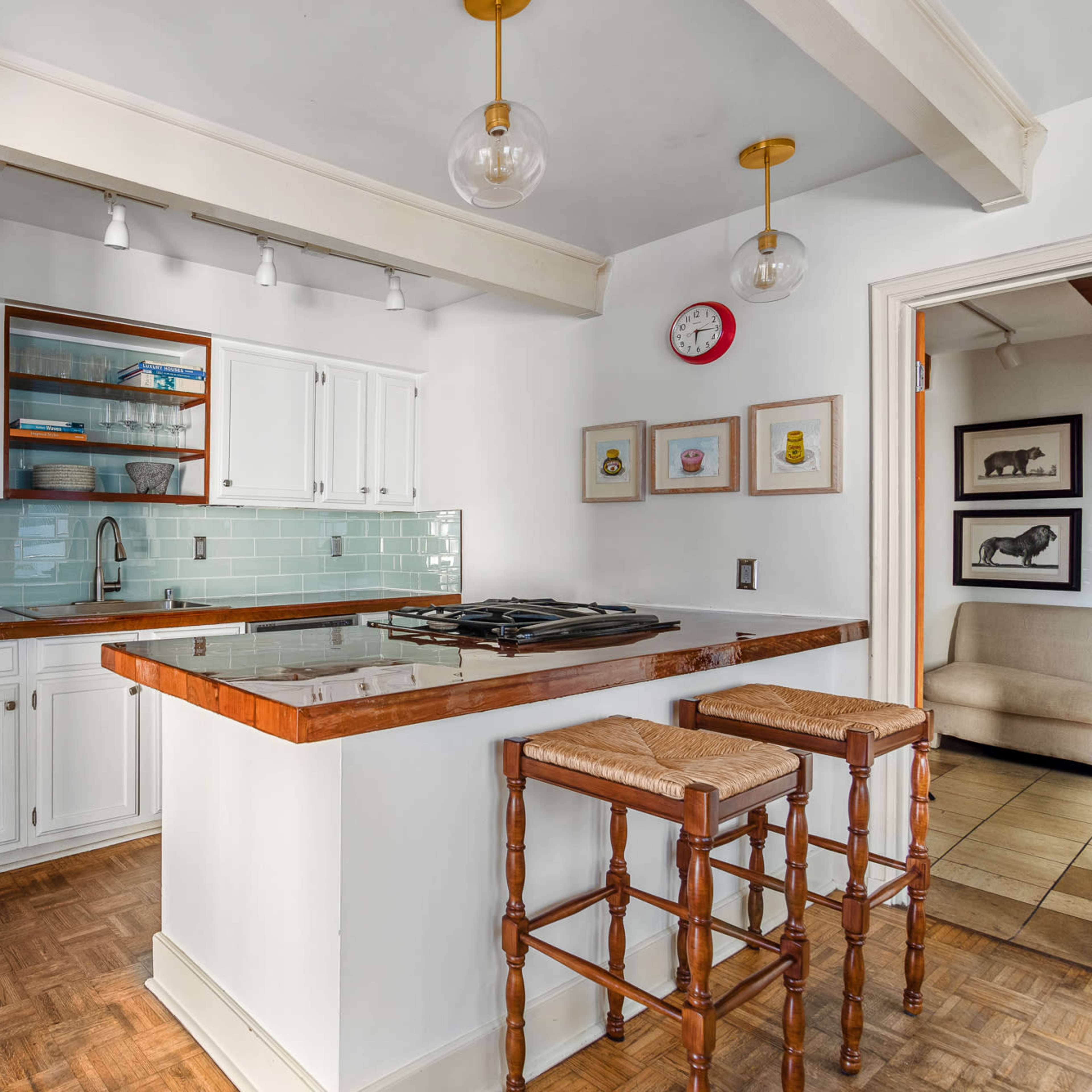A modern kitchen features stainless steel appliances, a tiled backsplash, and a breakfast bar with two wooden stools.