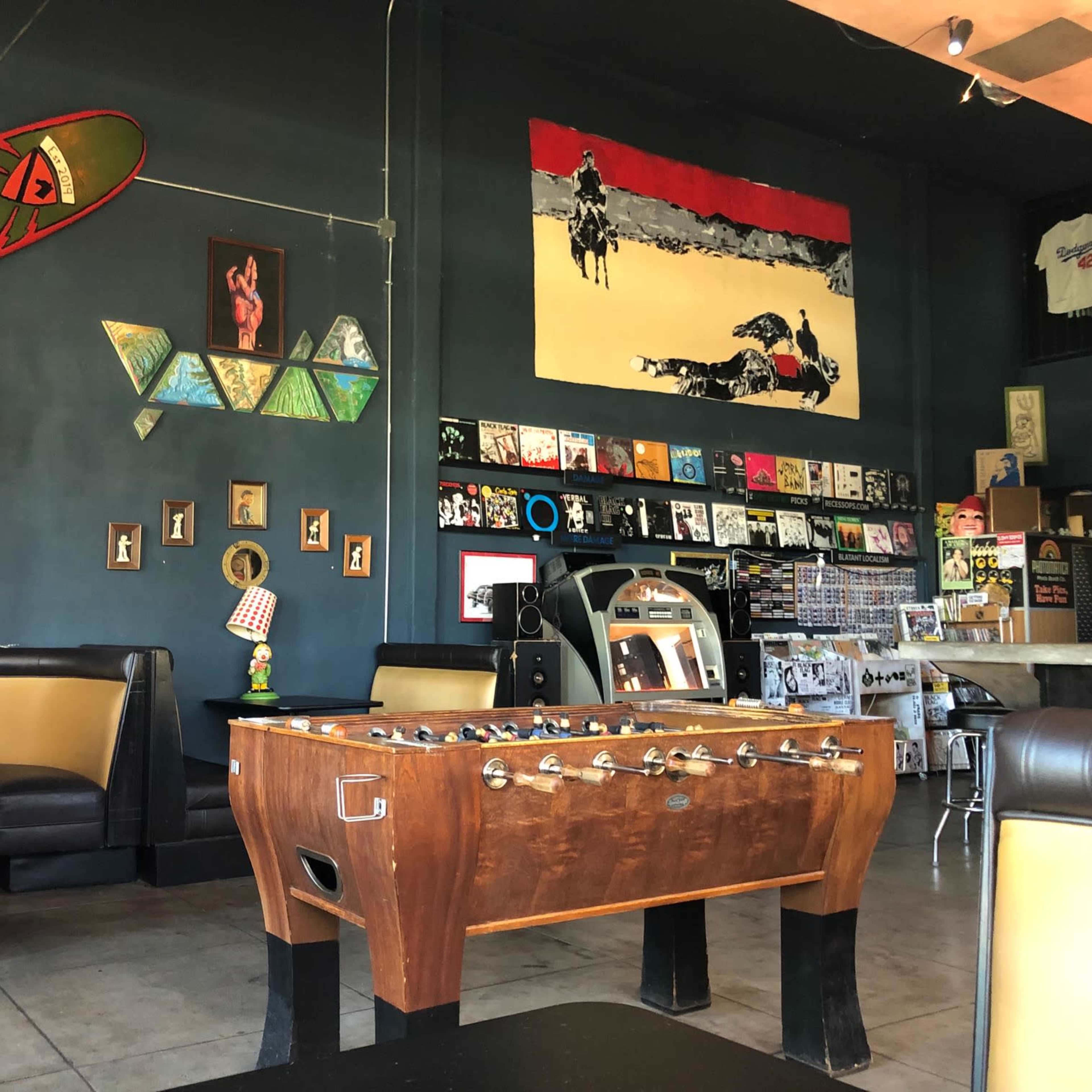 The interior of a casual bar or café featuring a foosball table, a large wall mural of a horse, and various framed artworks and records displayed on the walls.