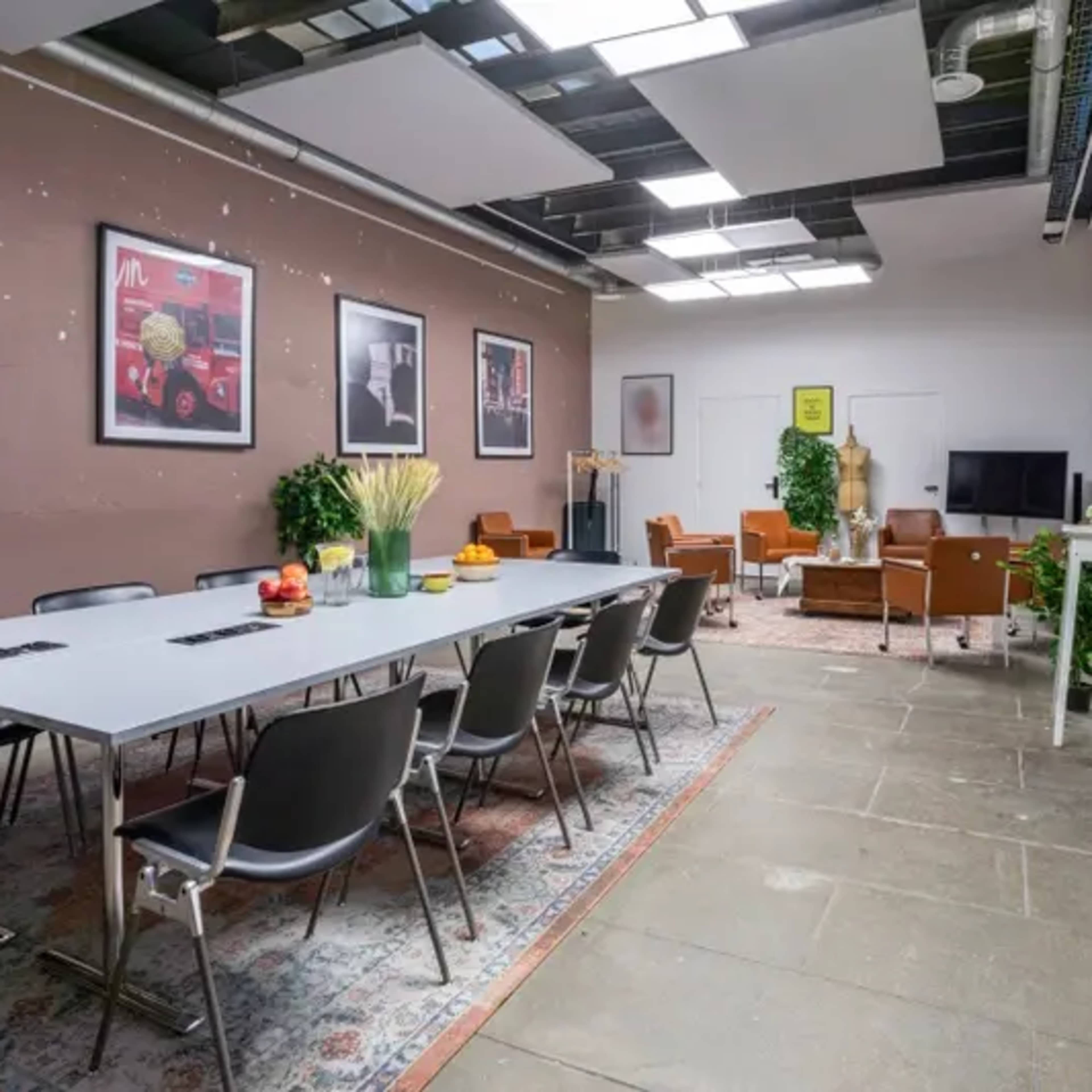 A modern meeting room features a long table surrounded by chairs, with artwork on the walls and a lounge area in the background.