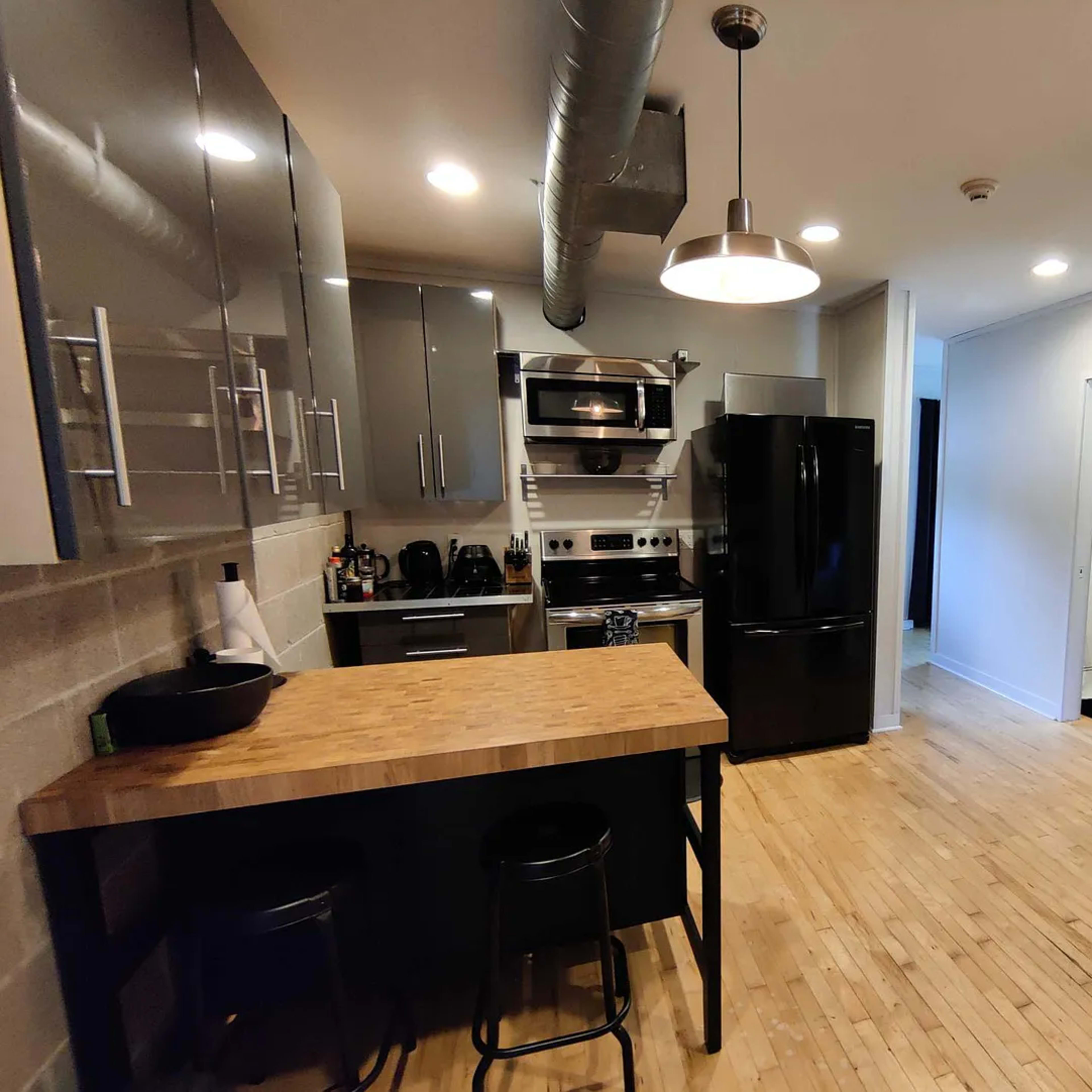 A modern kitchen with gray cabinets, a black refrigerator, and a wooden island with two black stools.
