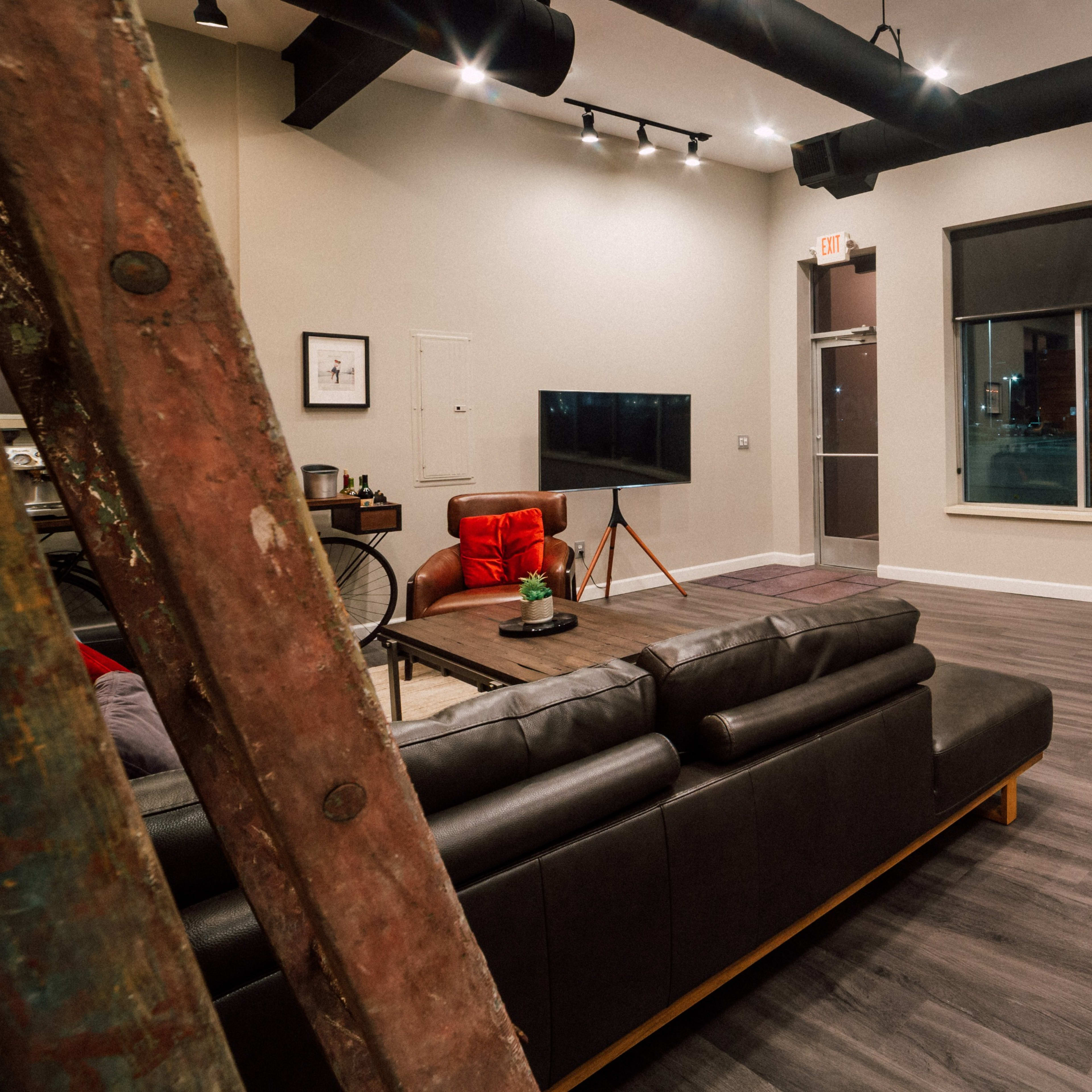A modern interior living area with a leather sofa, a coffee table, a red armchair, and a large window overlooking the street.
