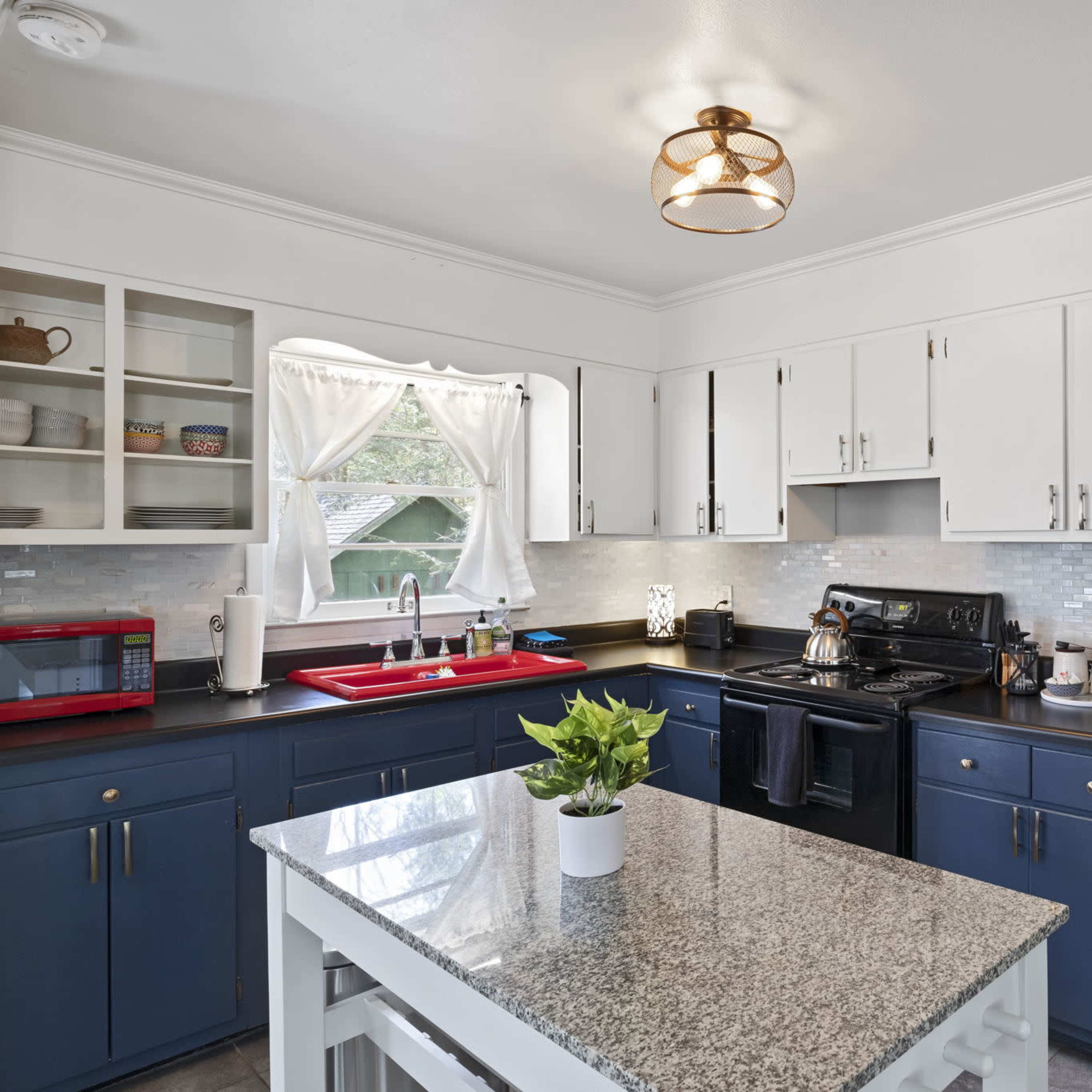 The kitchen features white cabinets, black appliances, a granite countertop island, and a window with sheer curtains.