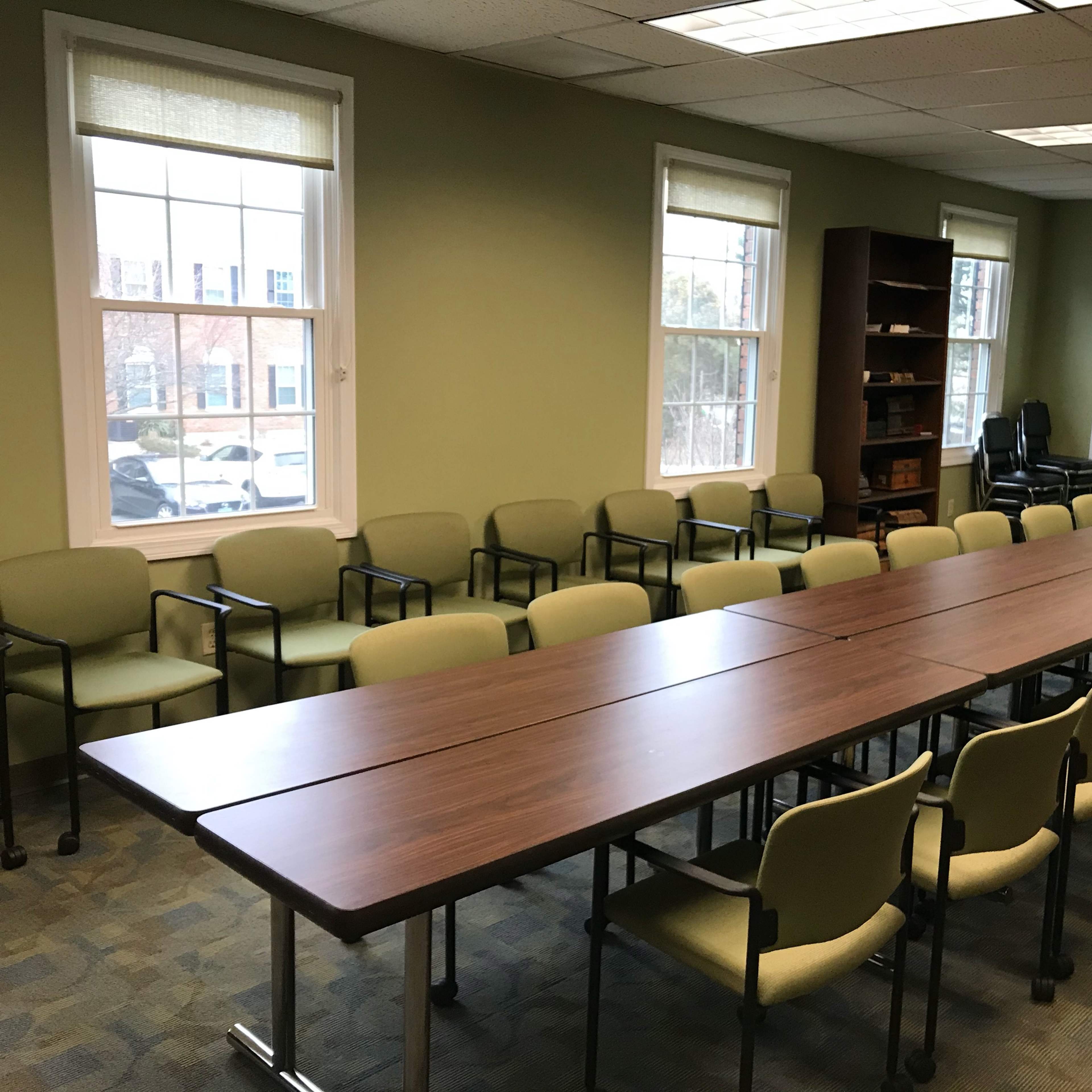 A conference room with a long wooden table surrounded by green chairs and large windows.