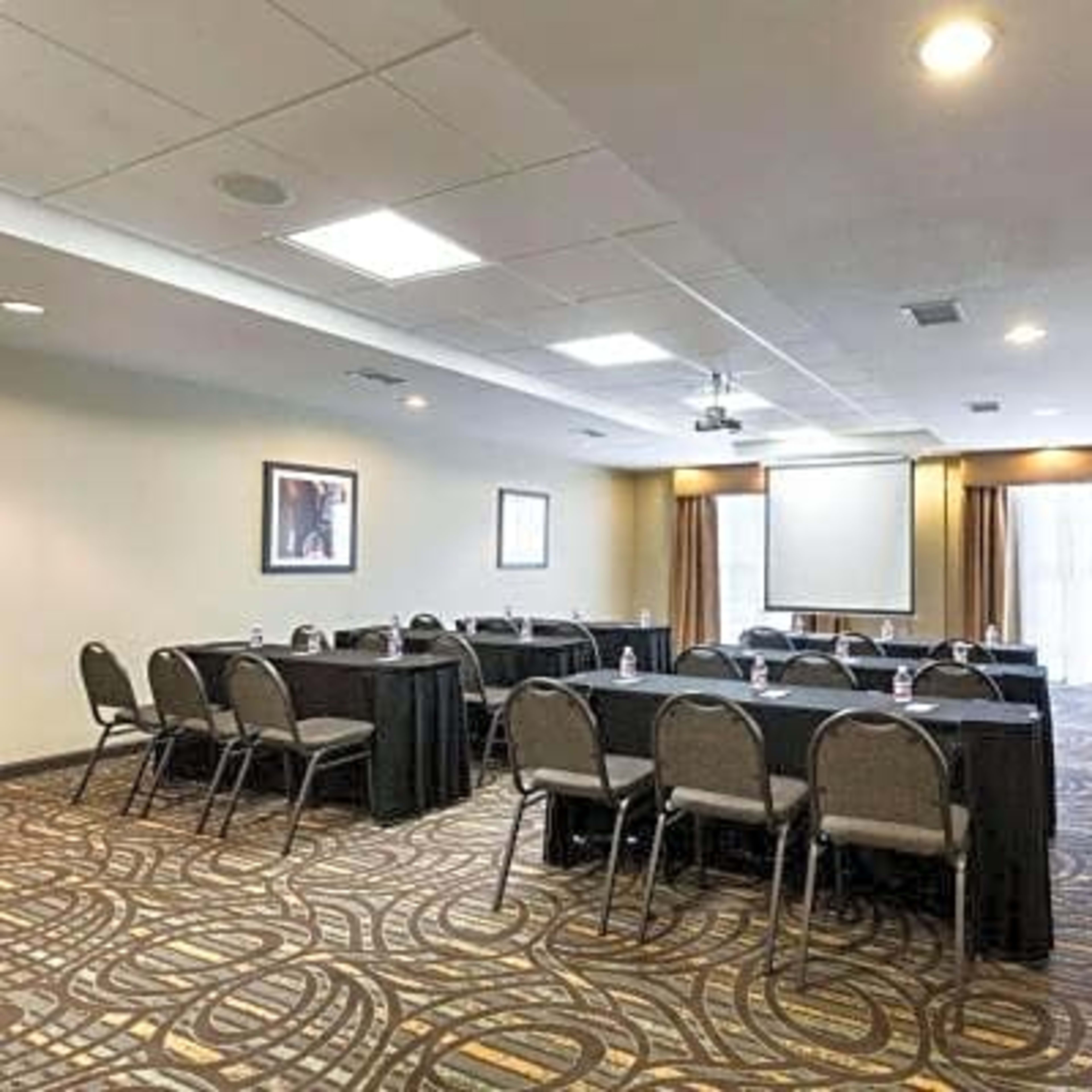 A conference room set up with multiple tables arranged in a U-shape, equipped with chairs and a projection screen at the front.