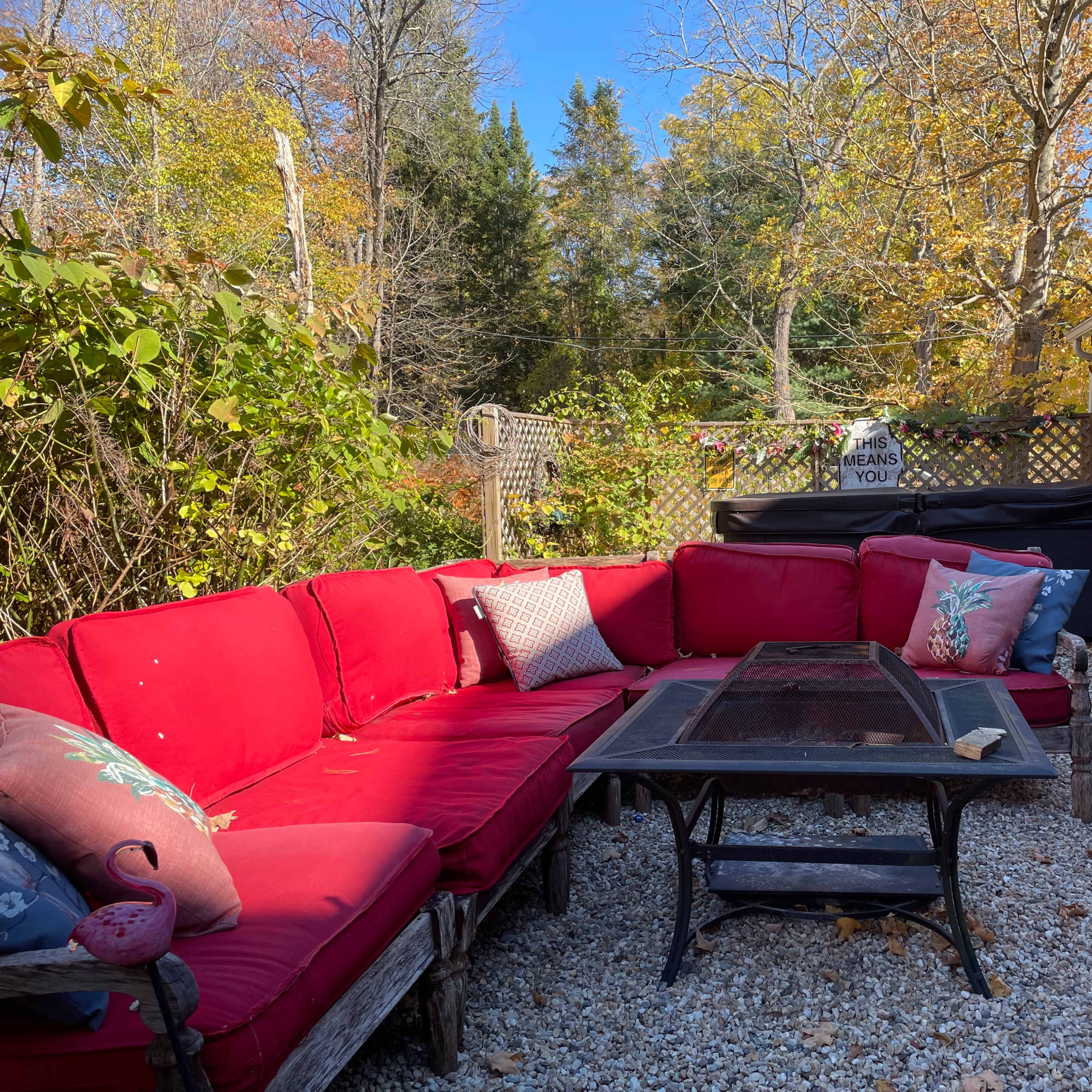 A red outdoor seating area with a large sectional sofa and a glass-top coffee table, surrounded by autumn foliage.