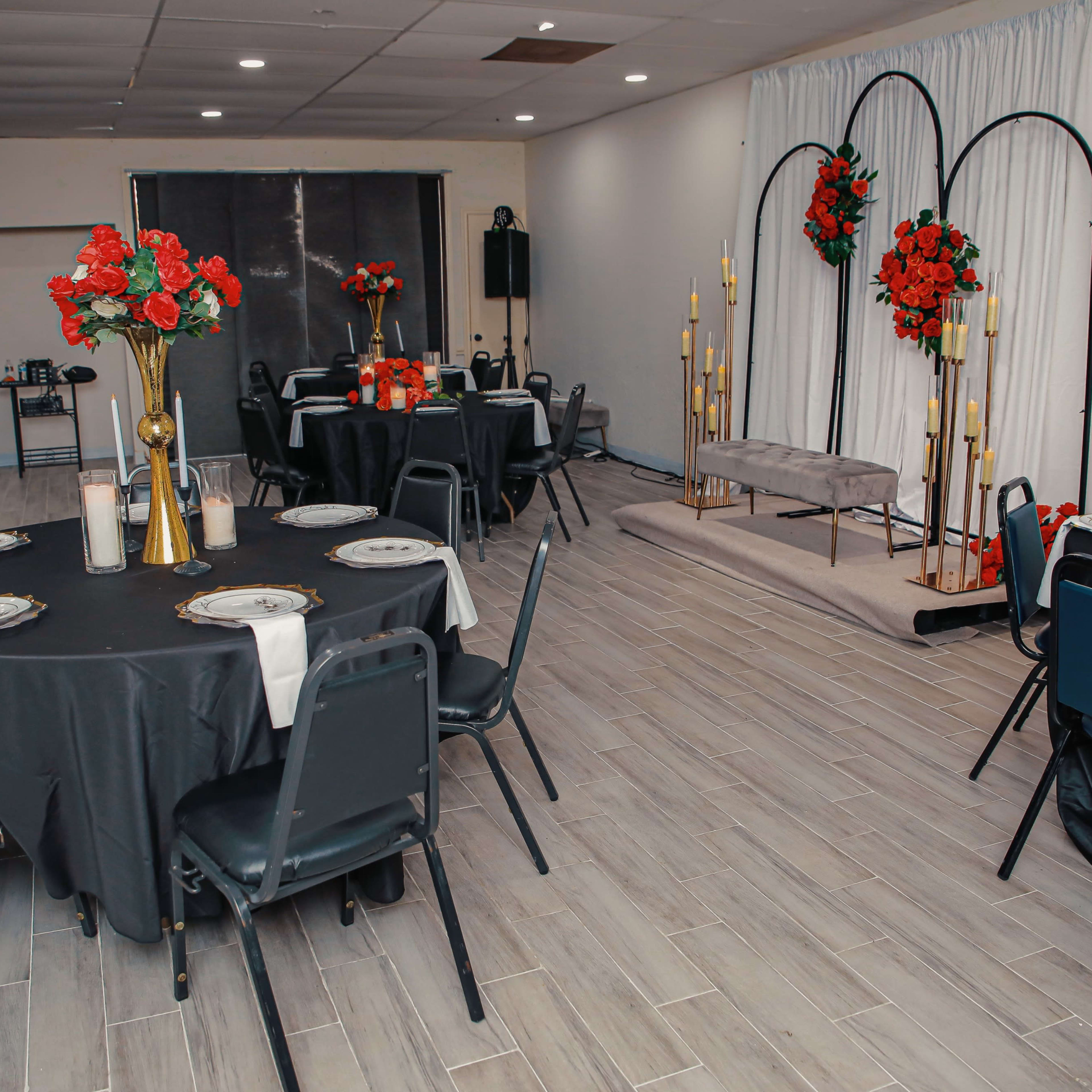 A banquet hall with black tables set for an event, featuring floral centerpieces and a backdrop of candles and floral arrangements.
