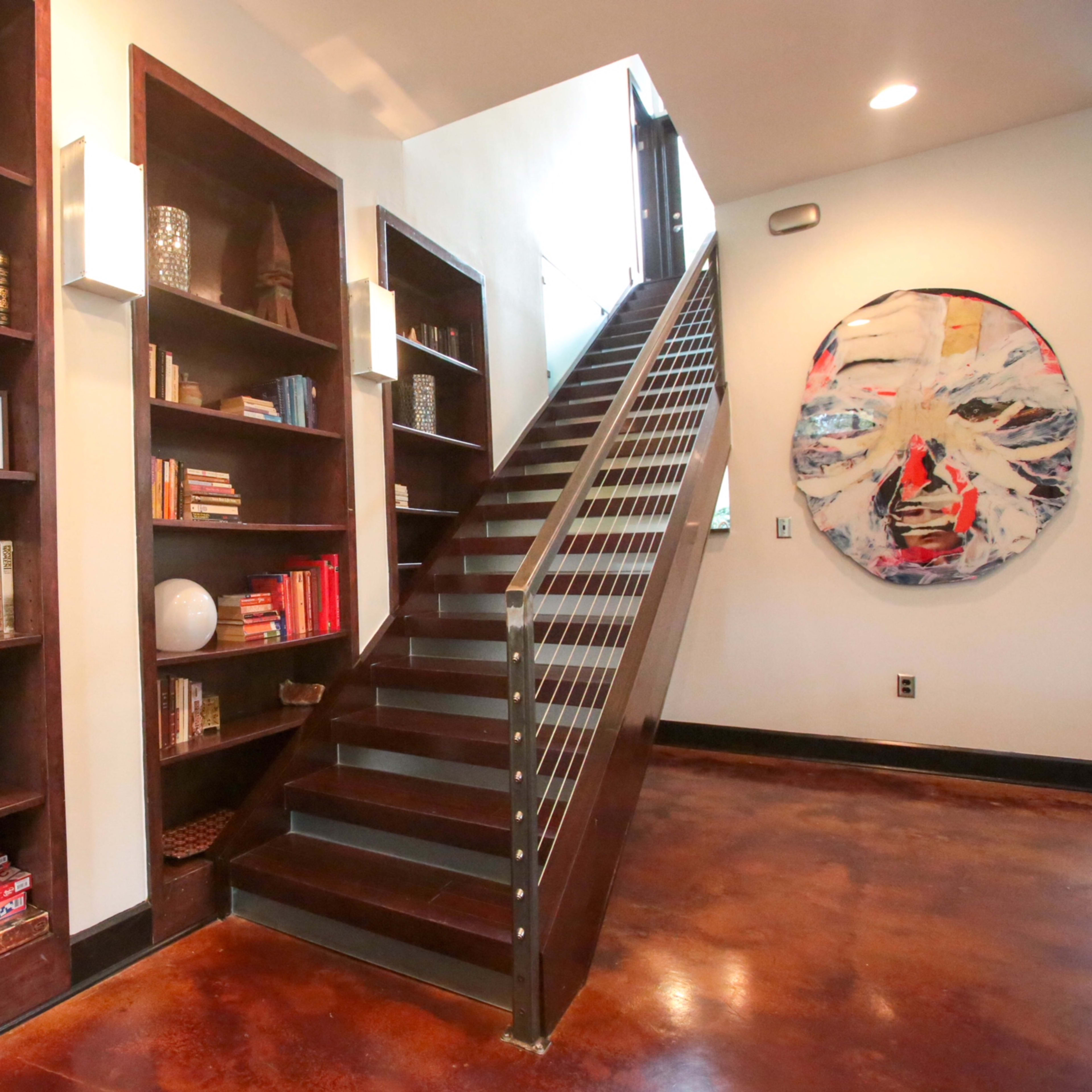 A modern hallway featuring built-in bookshelves filled with books, a plant, and a staircase leading to an upper level.