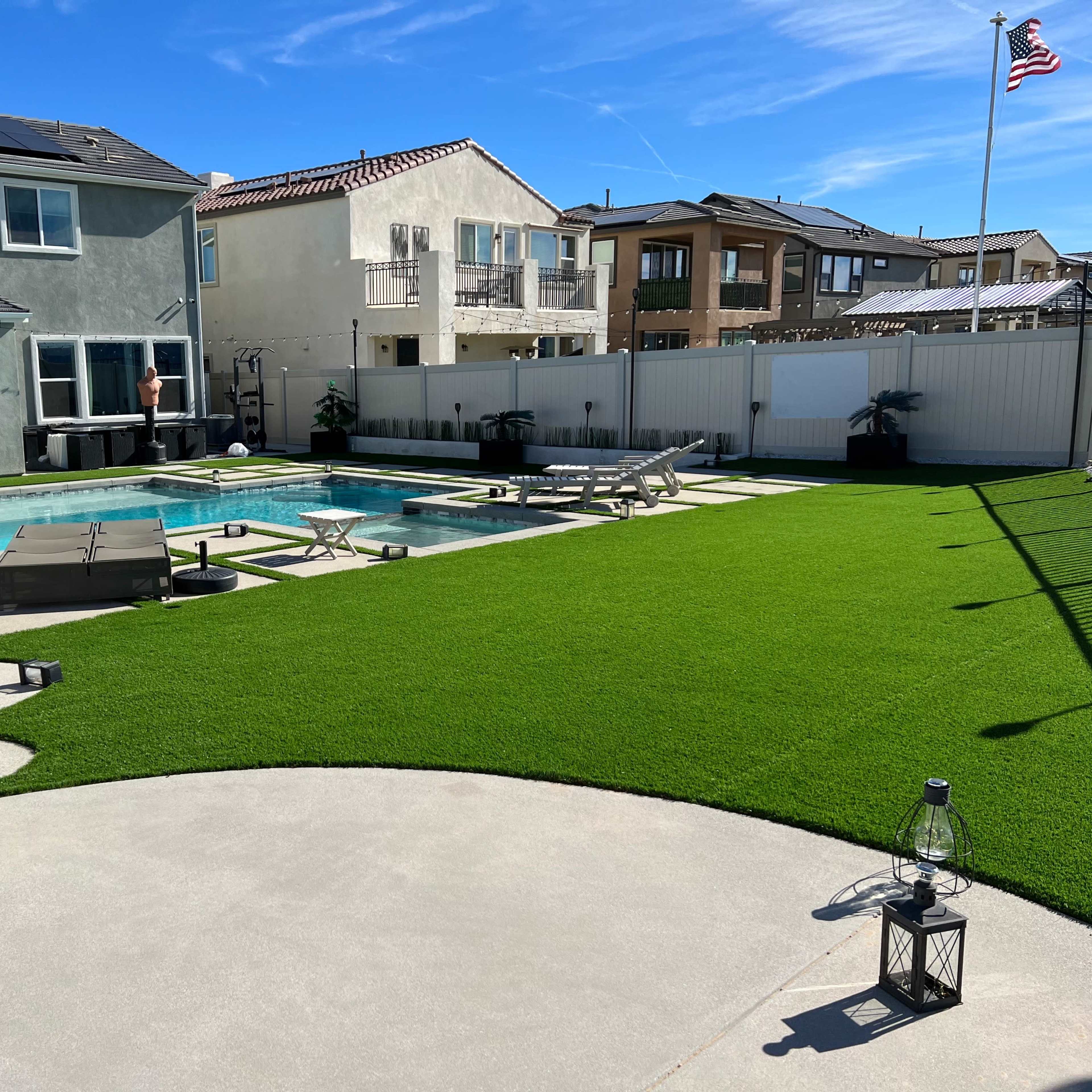 A backyard with a swimming pool surrounded by patio furniture, artificial grass, and a house in the background.
