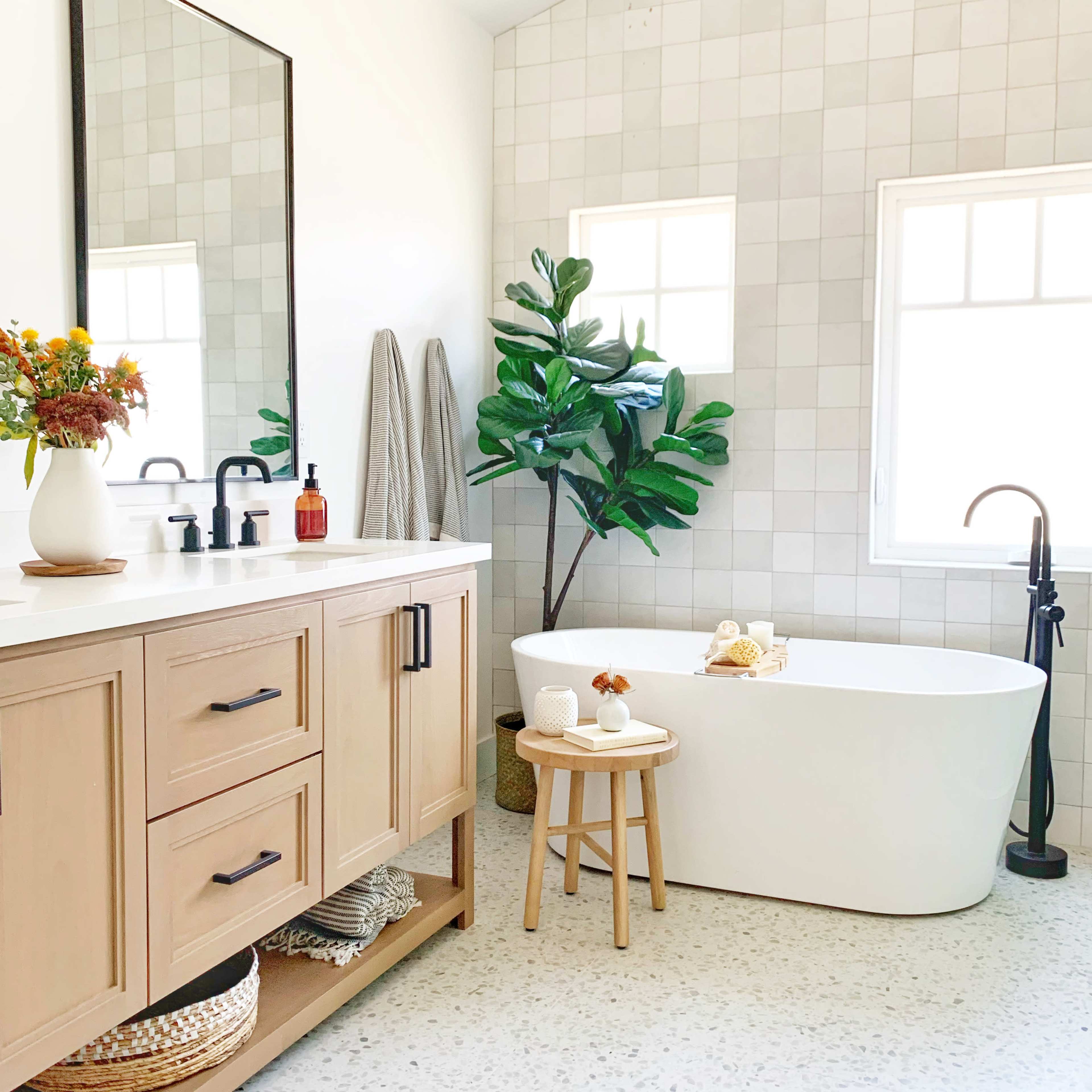 A modern bathroom featuring a freestanding white bathtub, a wooden vanity with a mirror, and decorative plants.