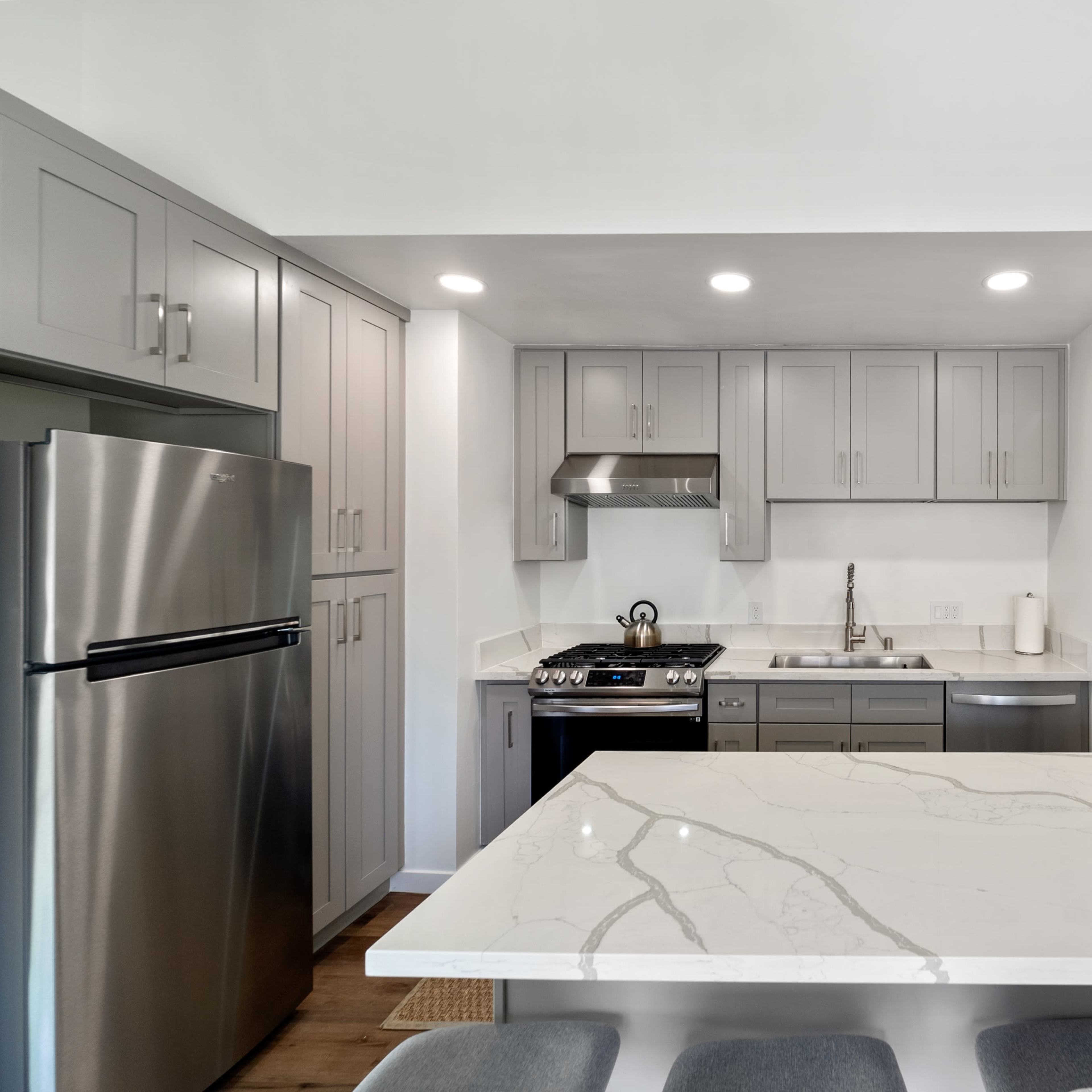 A modern kitchen features gray cabinetry, stainless steel appliances, and a large white marble countertop with seating.