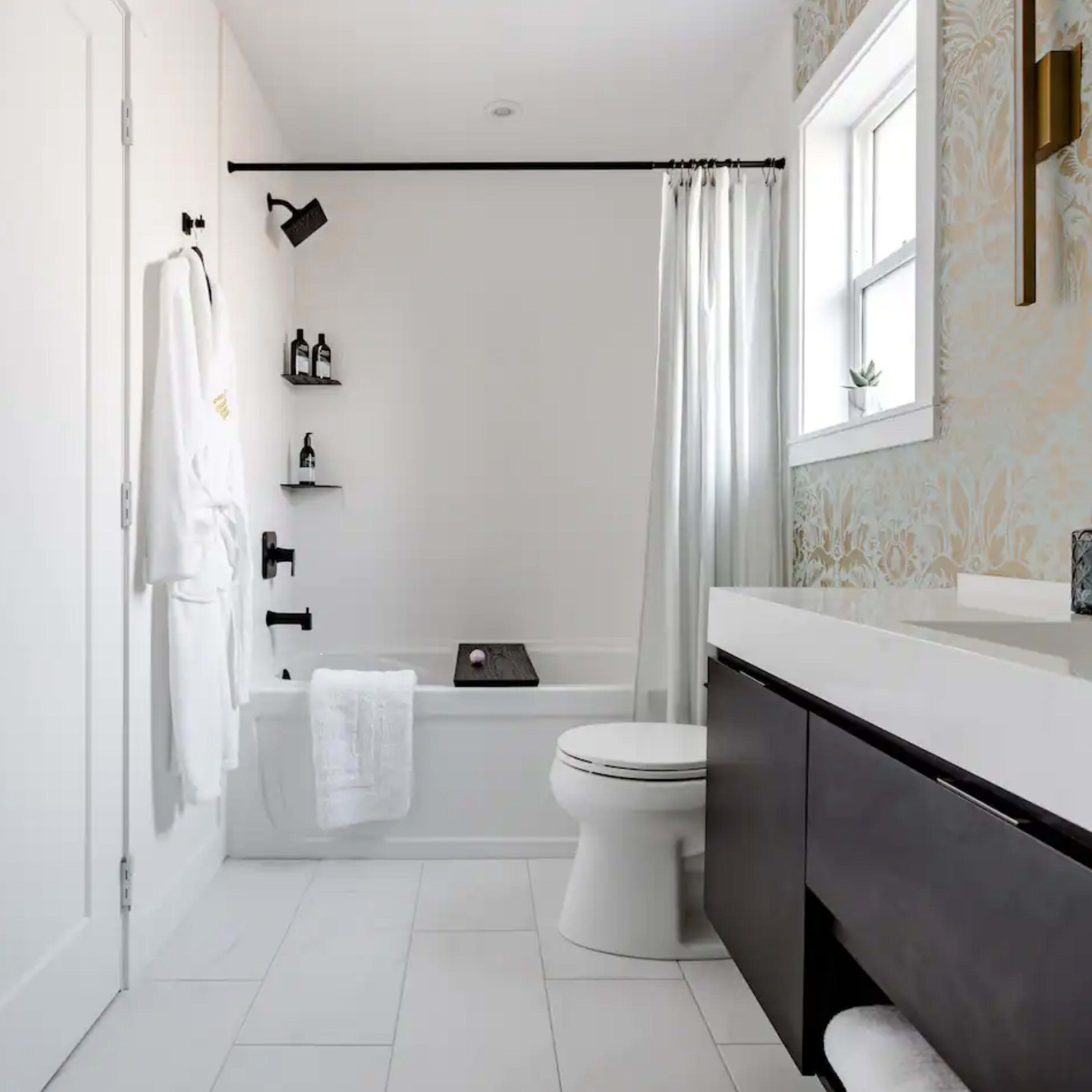 A modern bathroom featuring a bathtub, a wall-mounted mirror, a vanity with a sink, and white walls with an accent wallpaper.