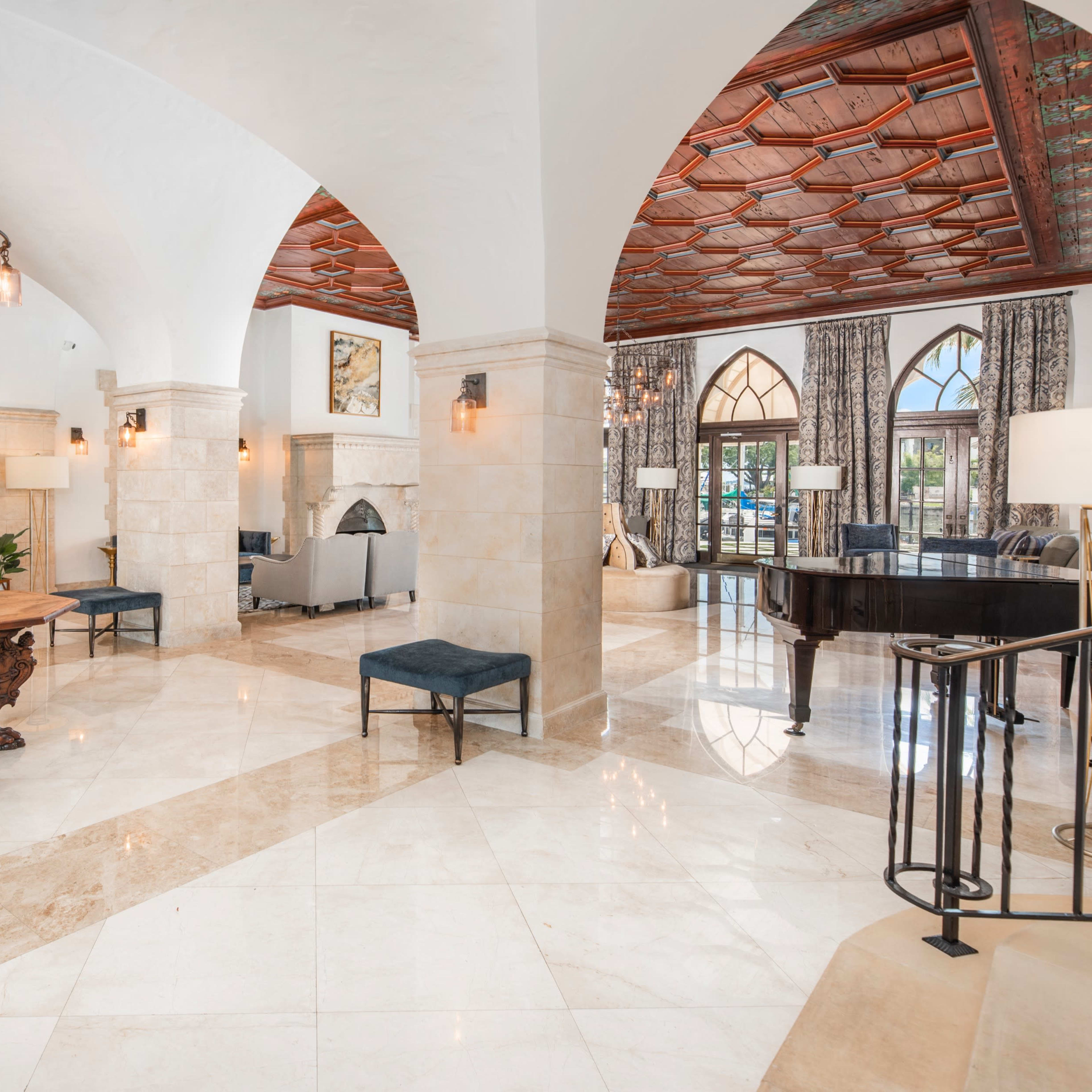 A spacious, elegantly designed lobby featuring high ceilings, marble flooring, and decorative arches, with a piano and seating areas arranged around a central table.