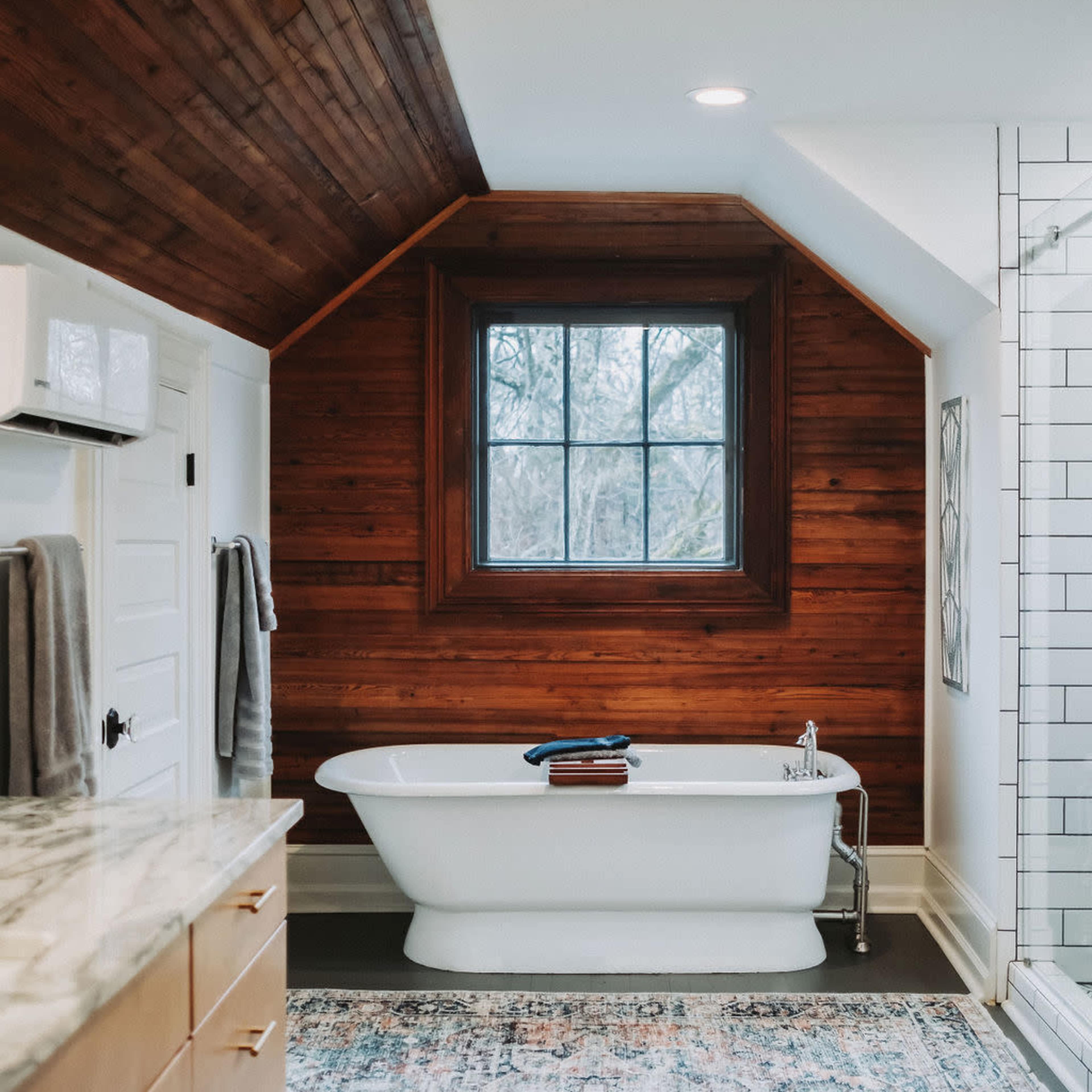 The bathroom features a freestanding bathtub under a large window, with wooden walls and a patterned rug on the floor.