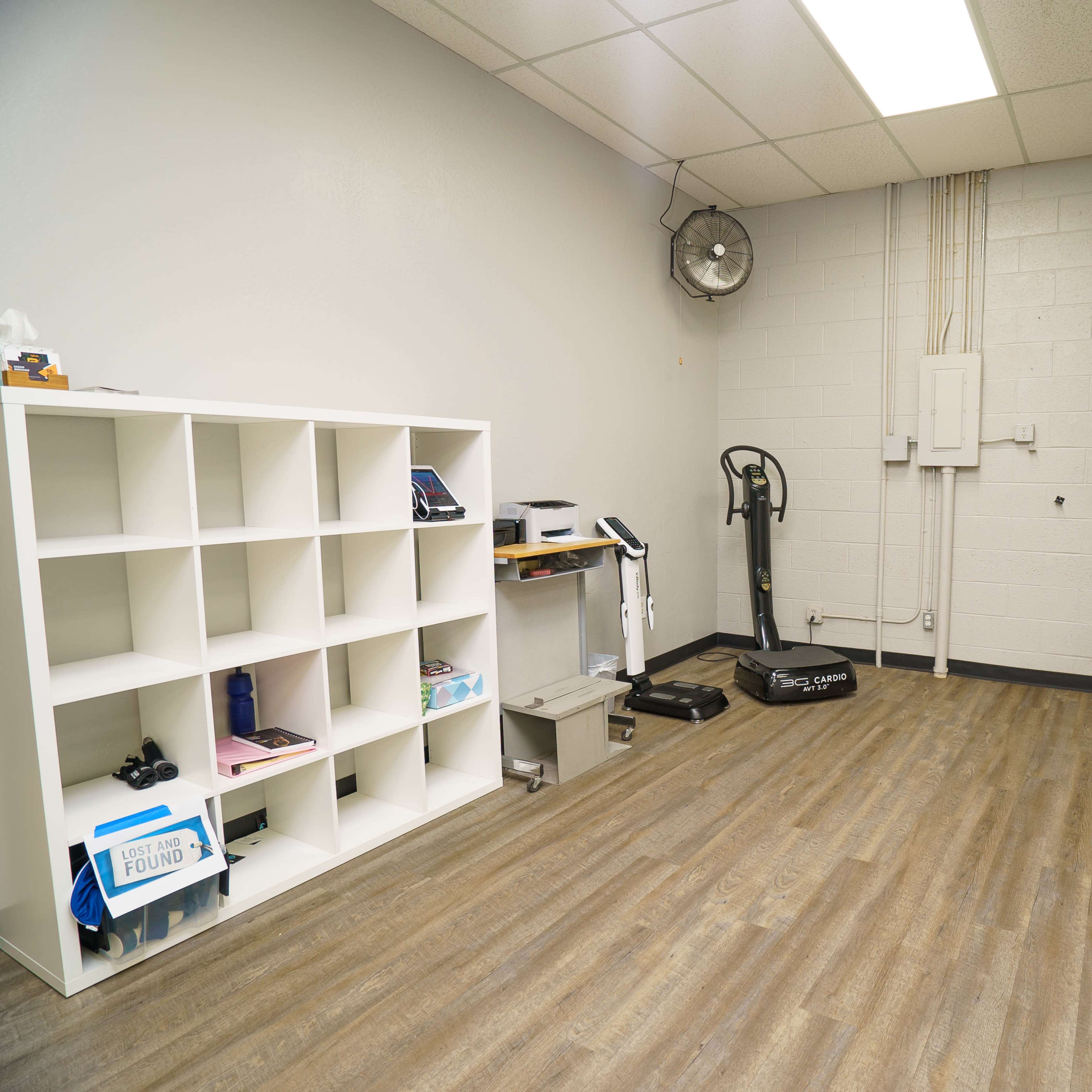 A sparsely furnished room with a cube shelving unit, a small exercise machine, and minimal decorations on the walls.
