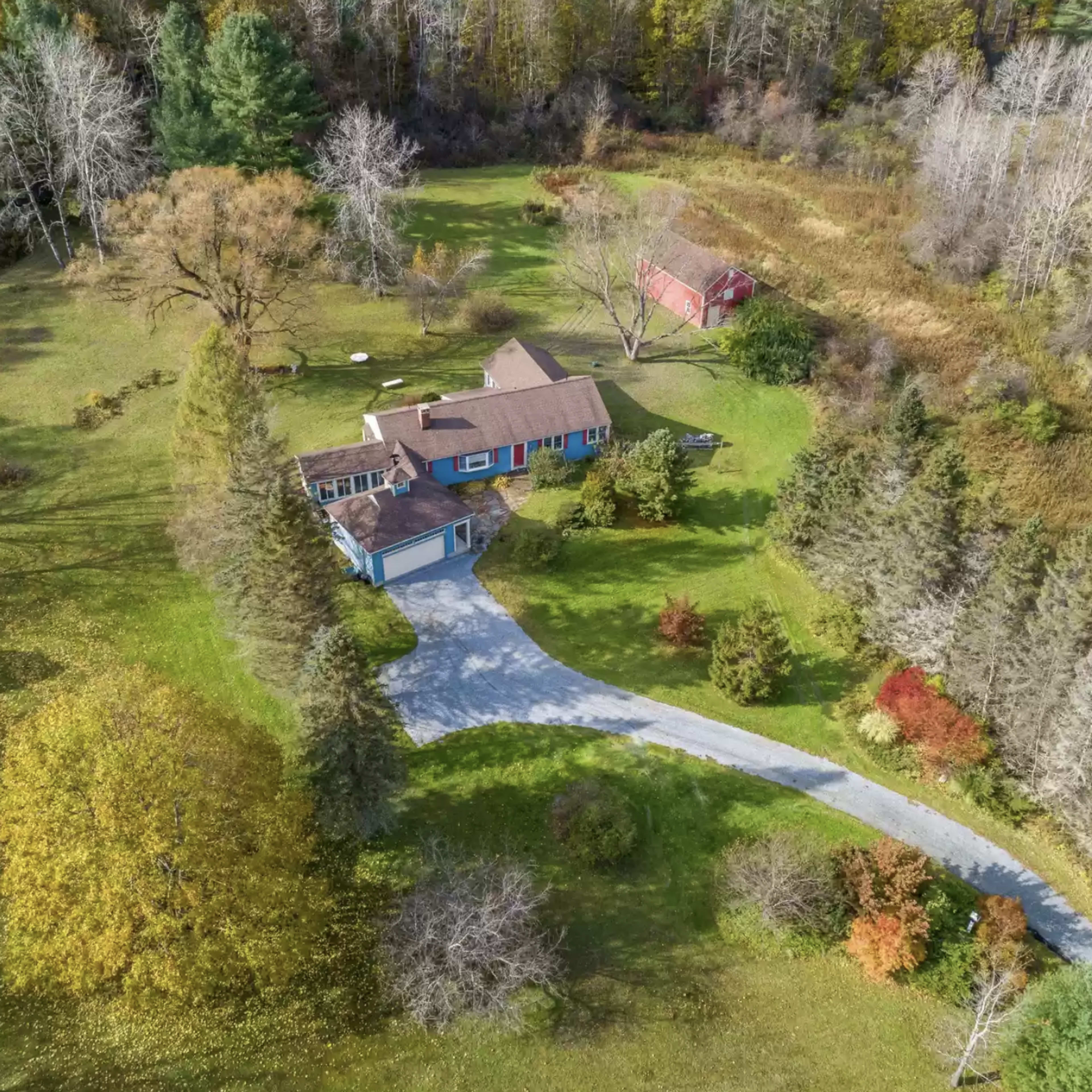 An aerial view of a house surrounded by trees and a winding driveway, with a barn-like structure in the background.