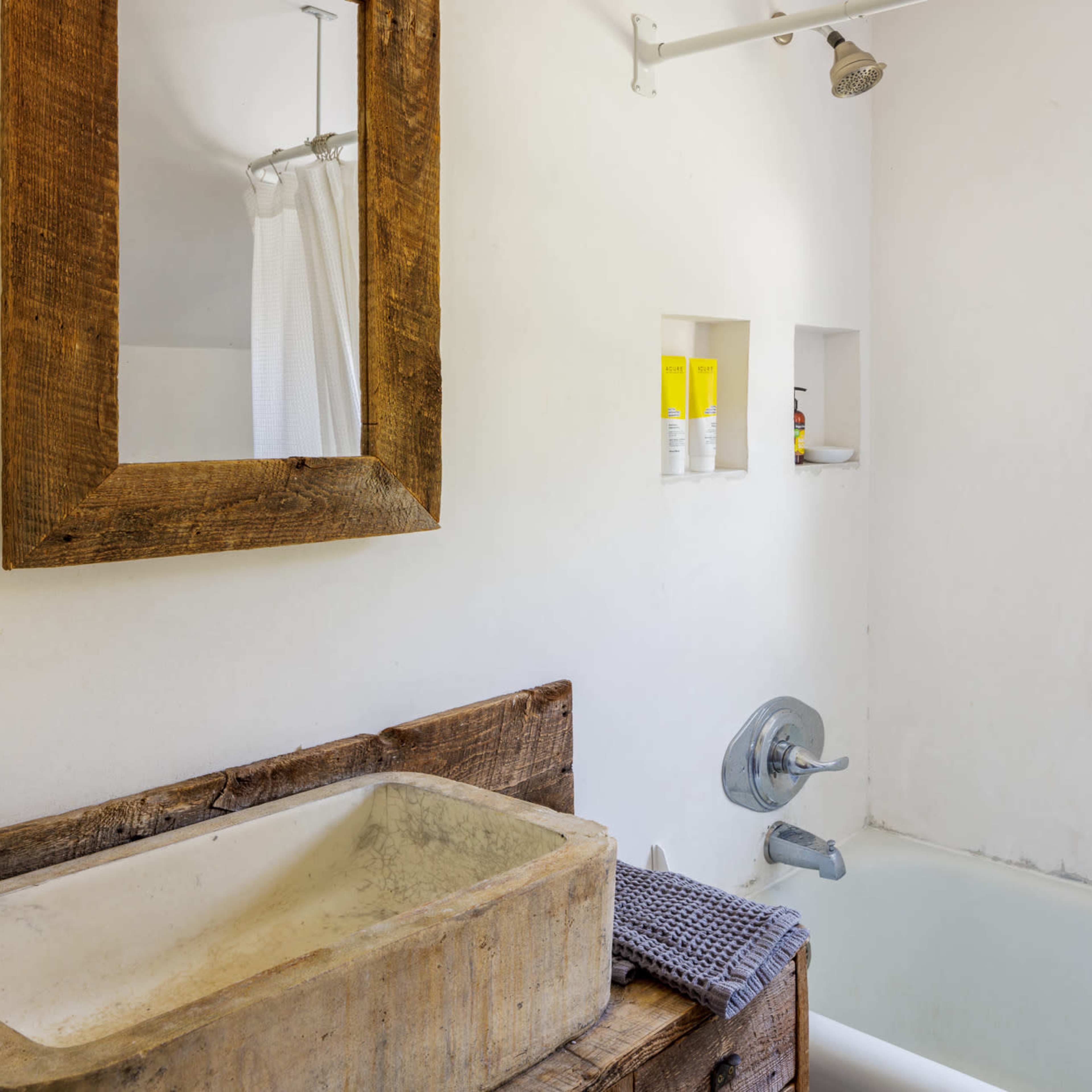 A simple bathroom featuring a wooden sink, a bathtub, a window with natural light, and a rustic mirror on the wall.