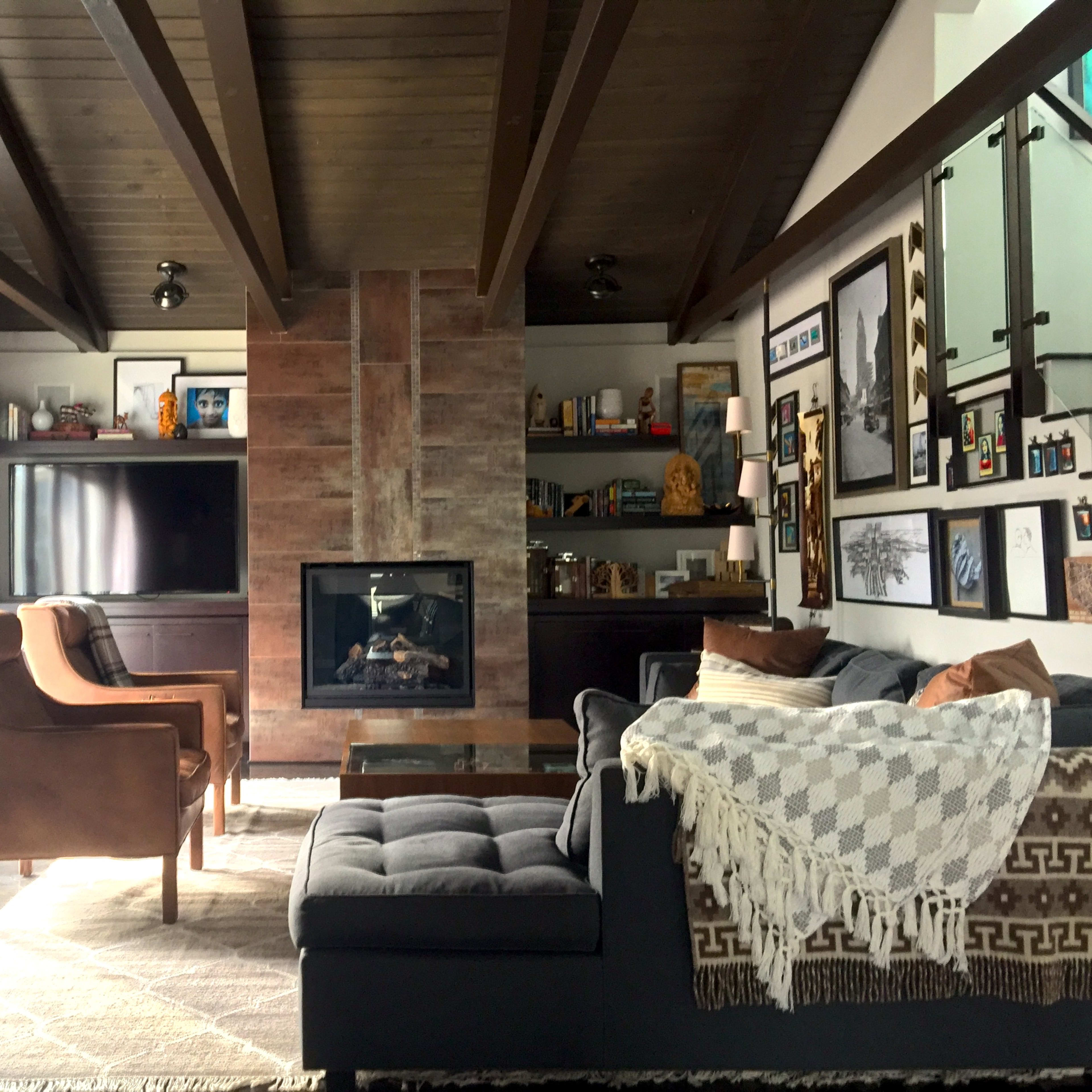 The living room features a sofa and armchairs arranged around a central coffee table, with a fireplace and shelves displaying decor in the background.