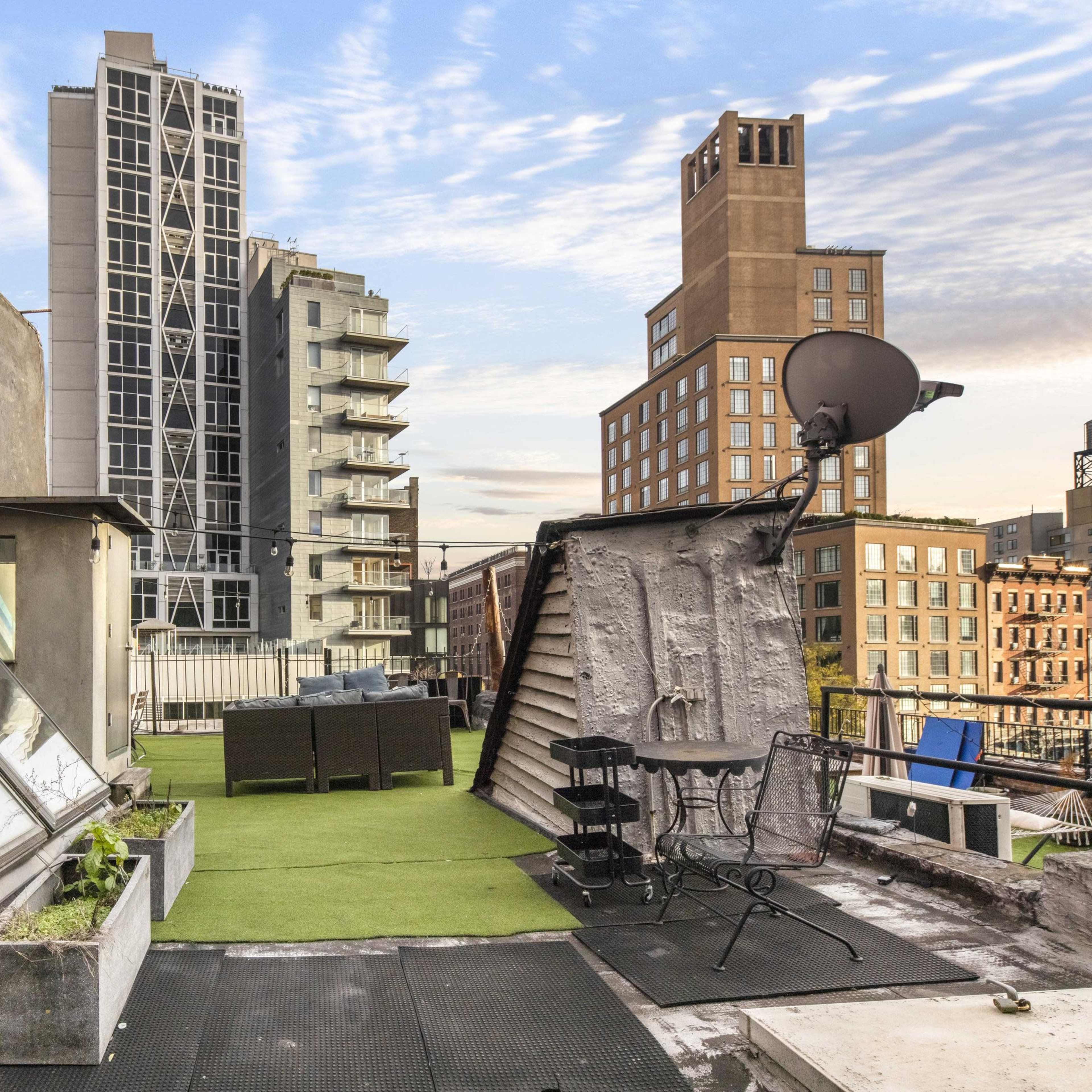 A rooftop terrace with modern buildings in the background, featuring skylights, planters, and outdoor furniture.