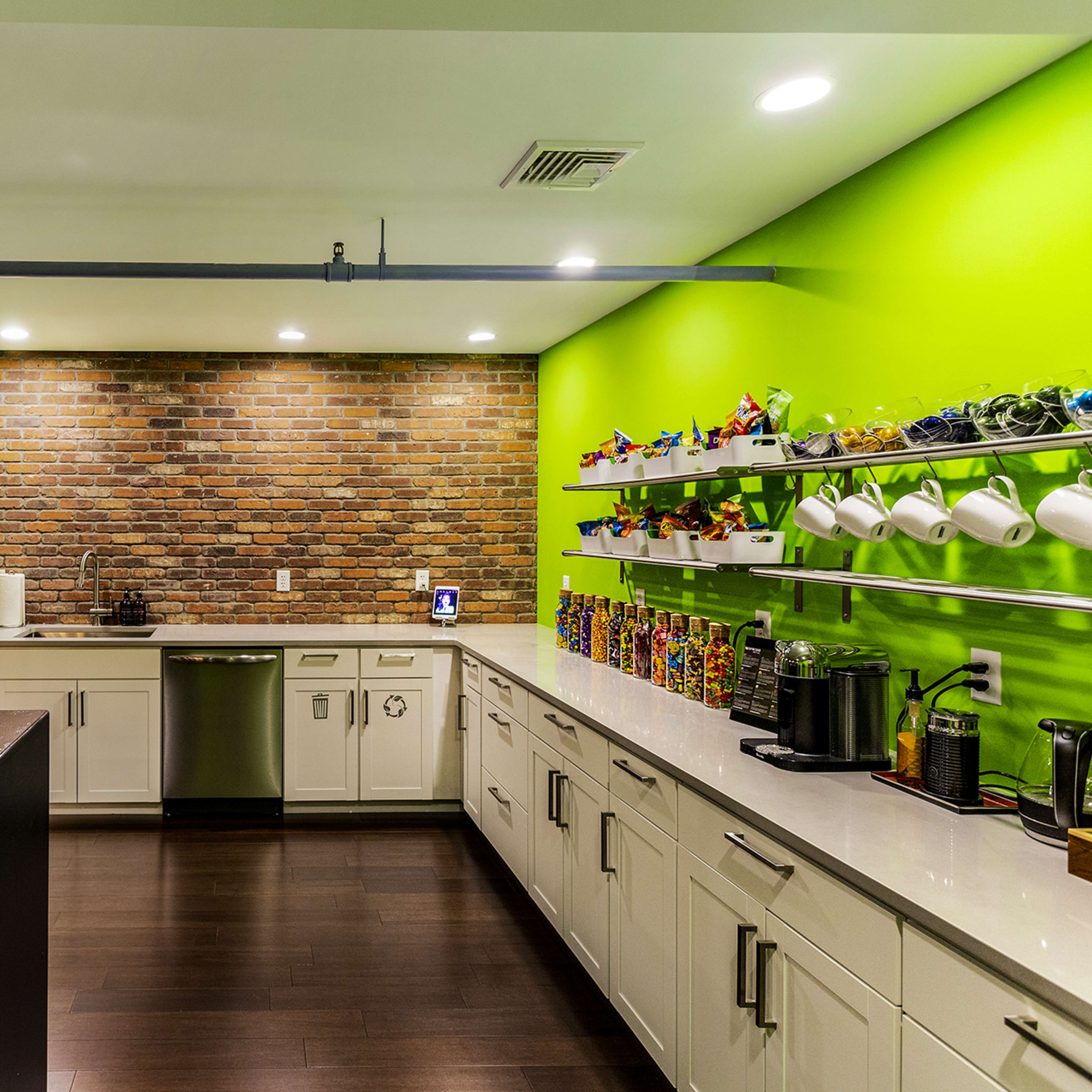 A modern kitchen with a green accent wall, brick backsplash, and white cabinetry, featuring a variety of kitchen appliances and colorful items on display.