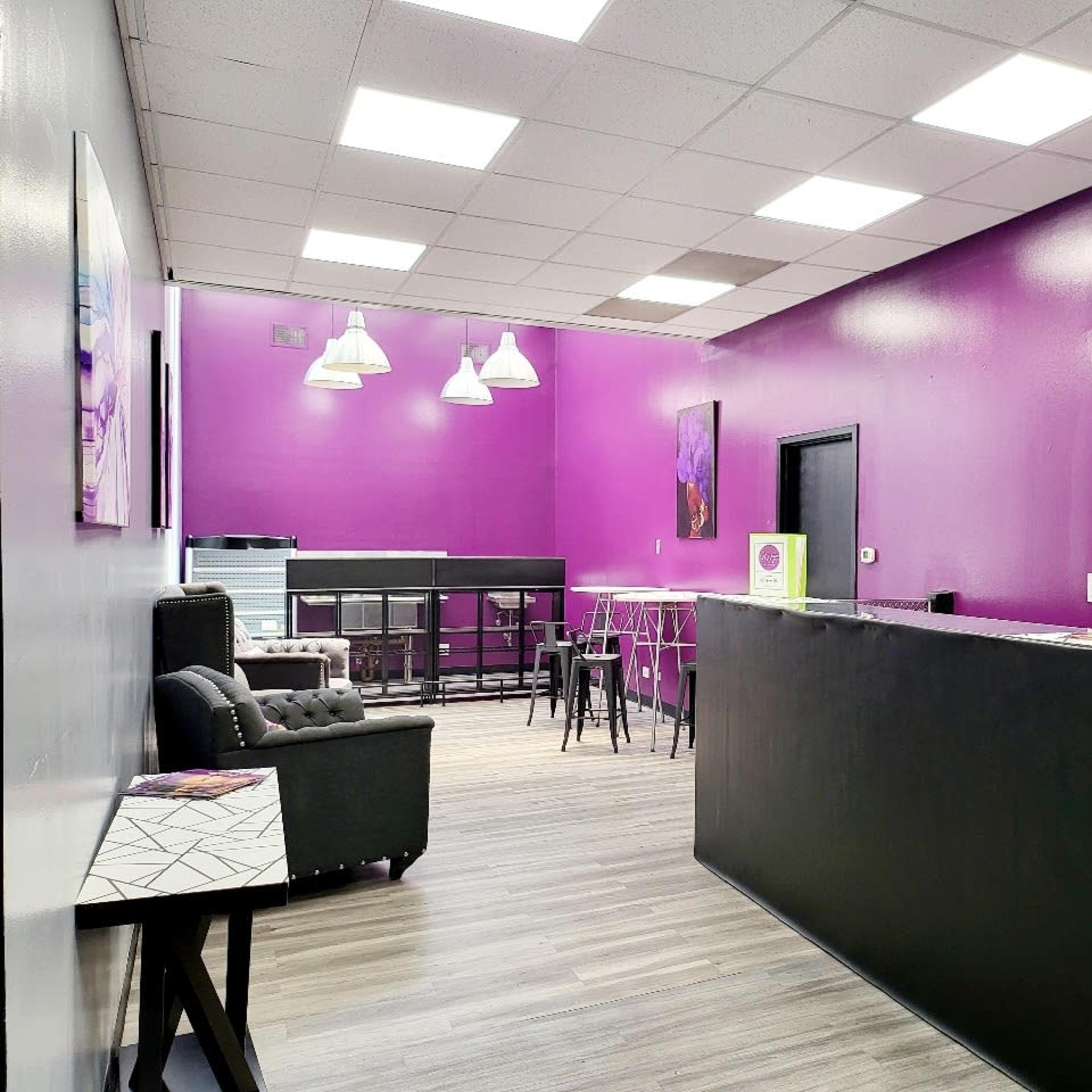 A brightly colored waiting area with purple walls, a reception desk, seating, and tables in a modern design.