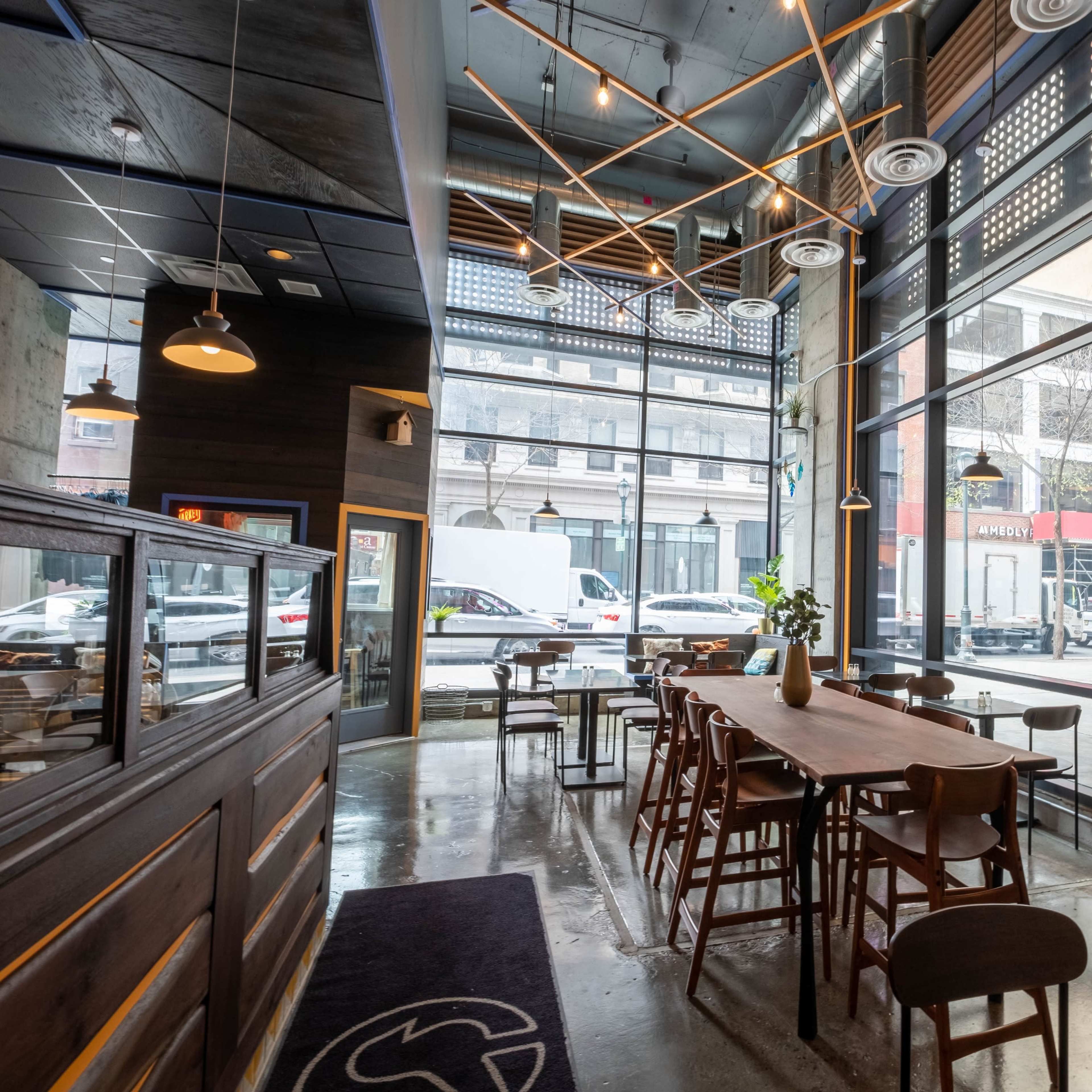 A modern café features large windows, wooden tables, and a minimalist interior design.