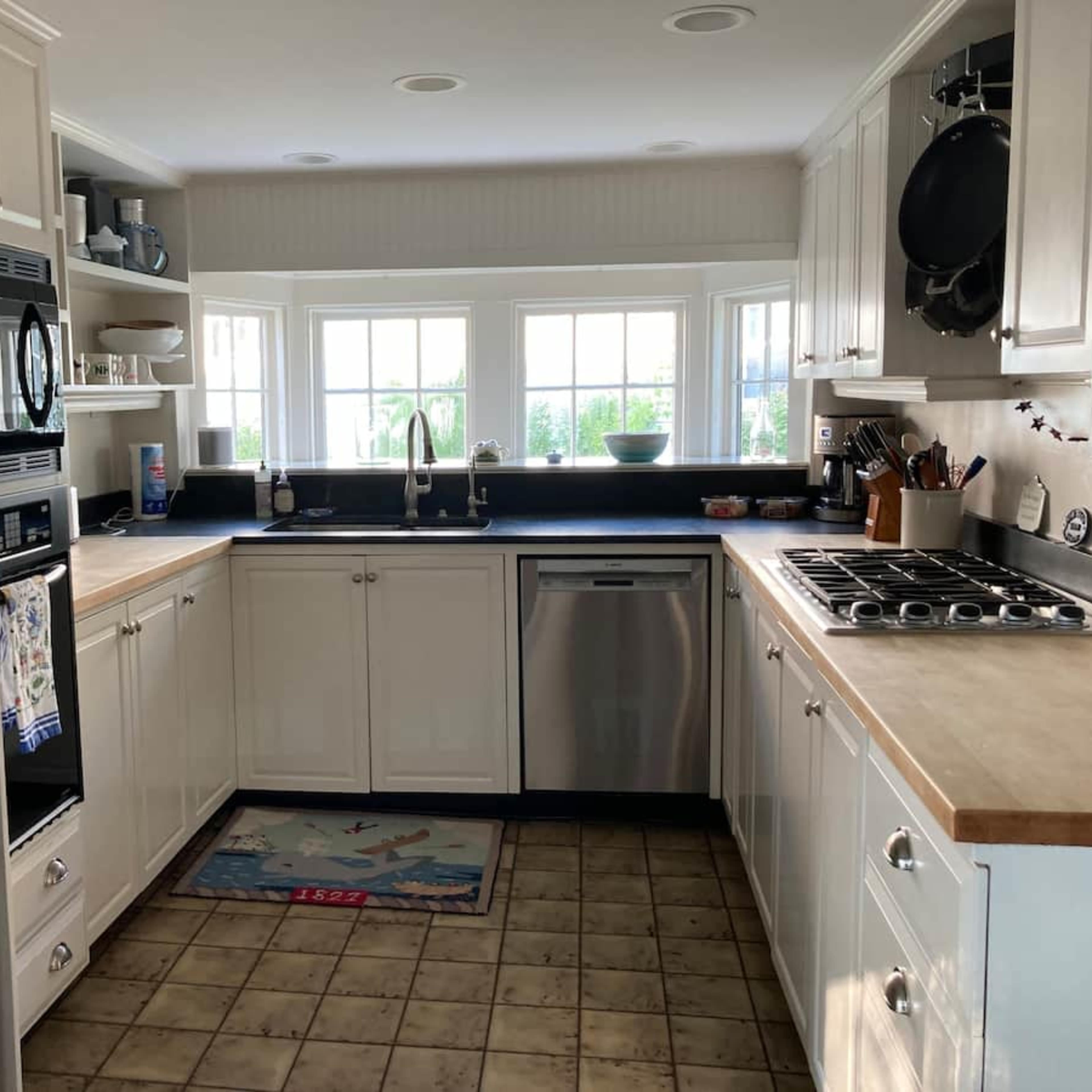 A modern kitchen with white cabinetry, a stainless steel refrigerator, and a countertop under a window with a view.
