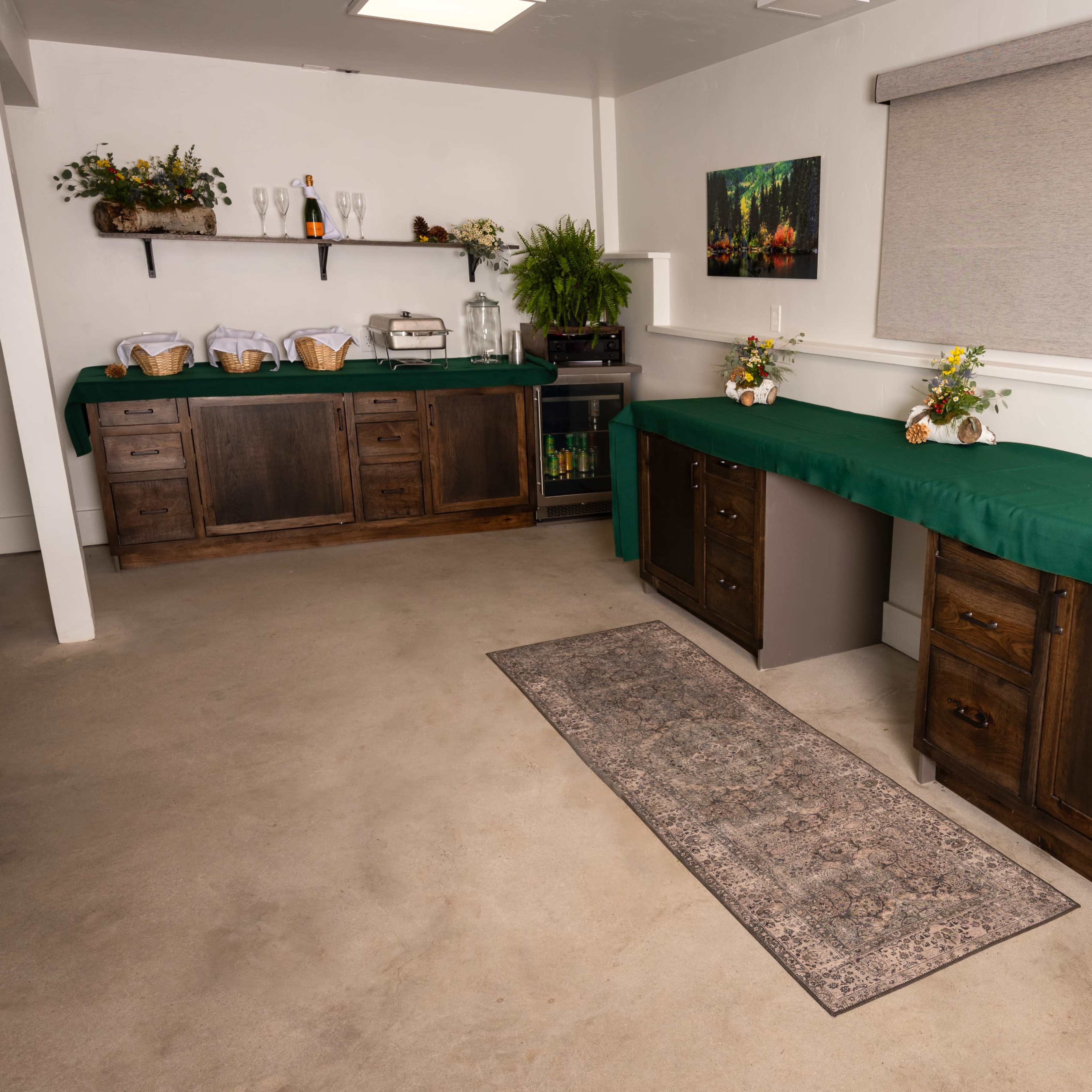 A room with two wooden cabinets covered by green tablecloths, a decorative area with potted plants, and a rug on the floor.
