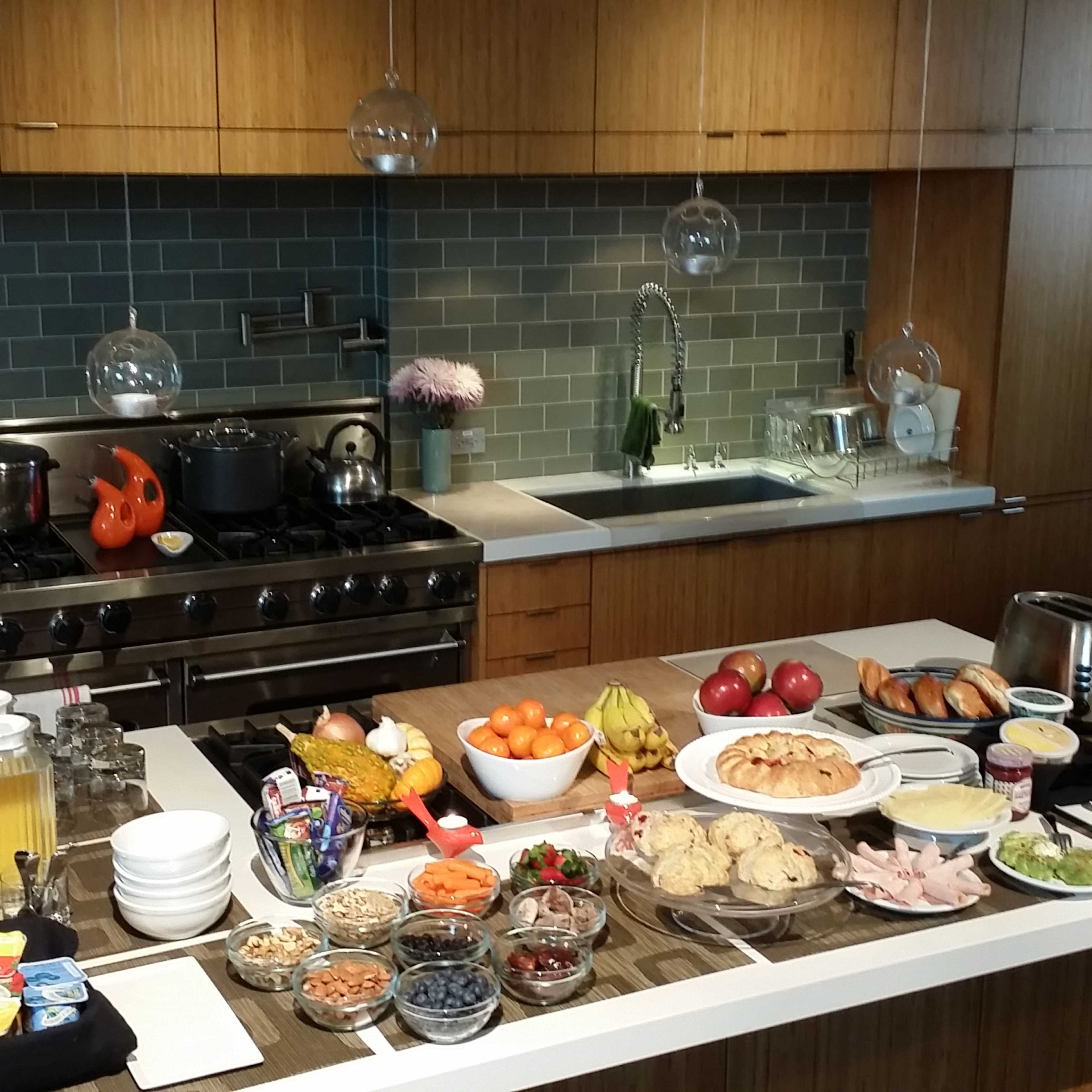 A kitchen counter filled with a variety of food items, including pastries, fruits, snacks, and beverages, arranged for a meal or gathering.