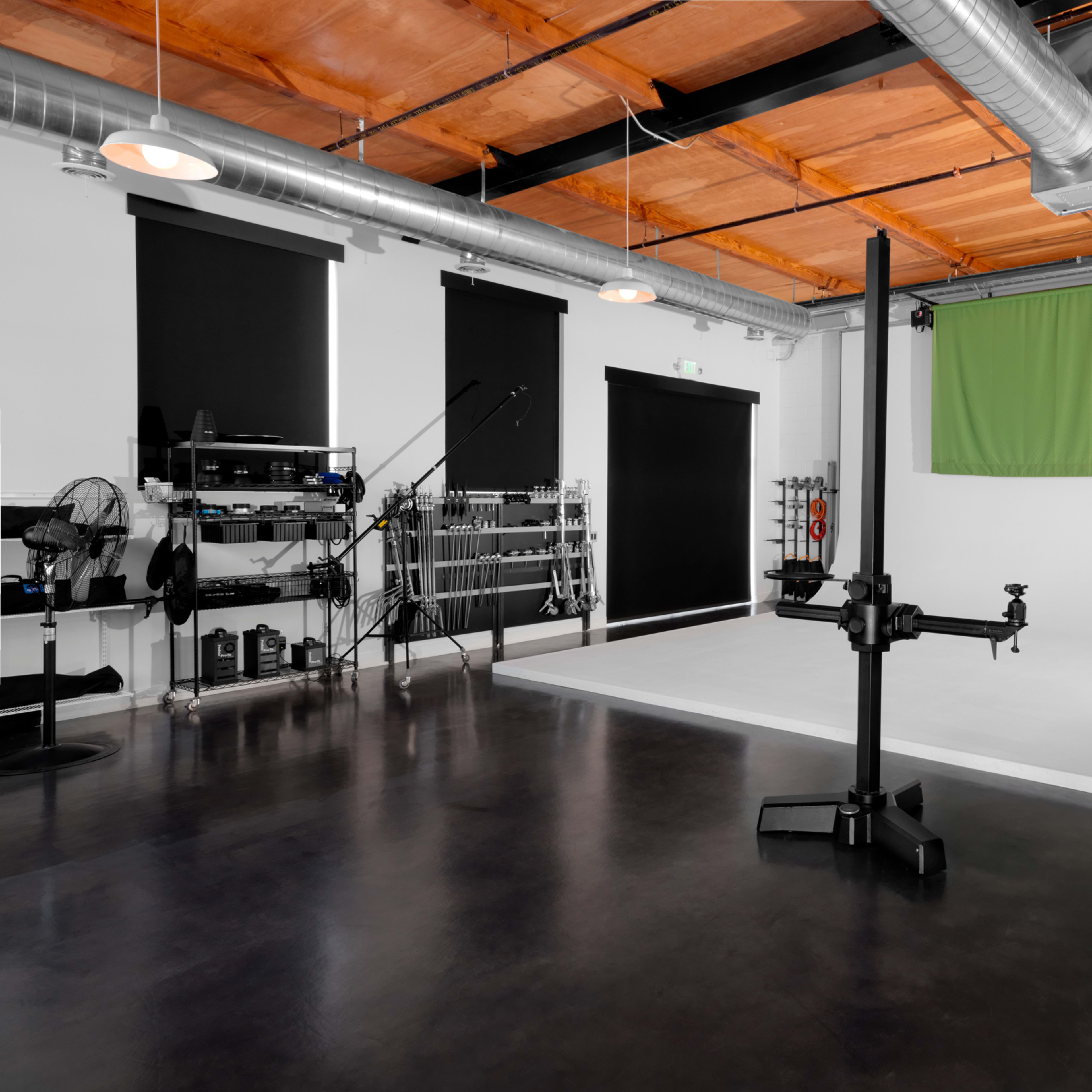 A spacious photography studio with a white backdrop, green screen, and various equipment arranged along the walls.