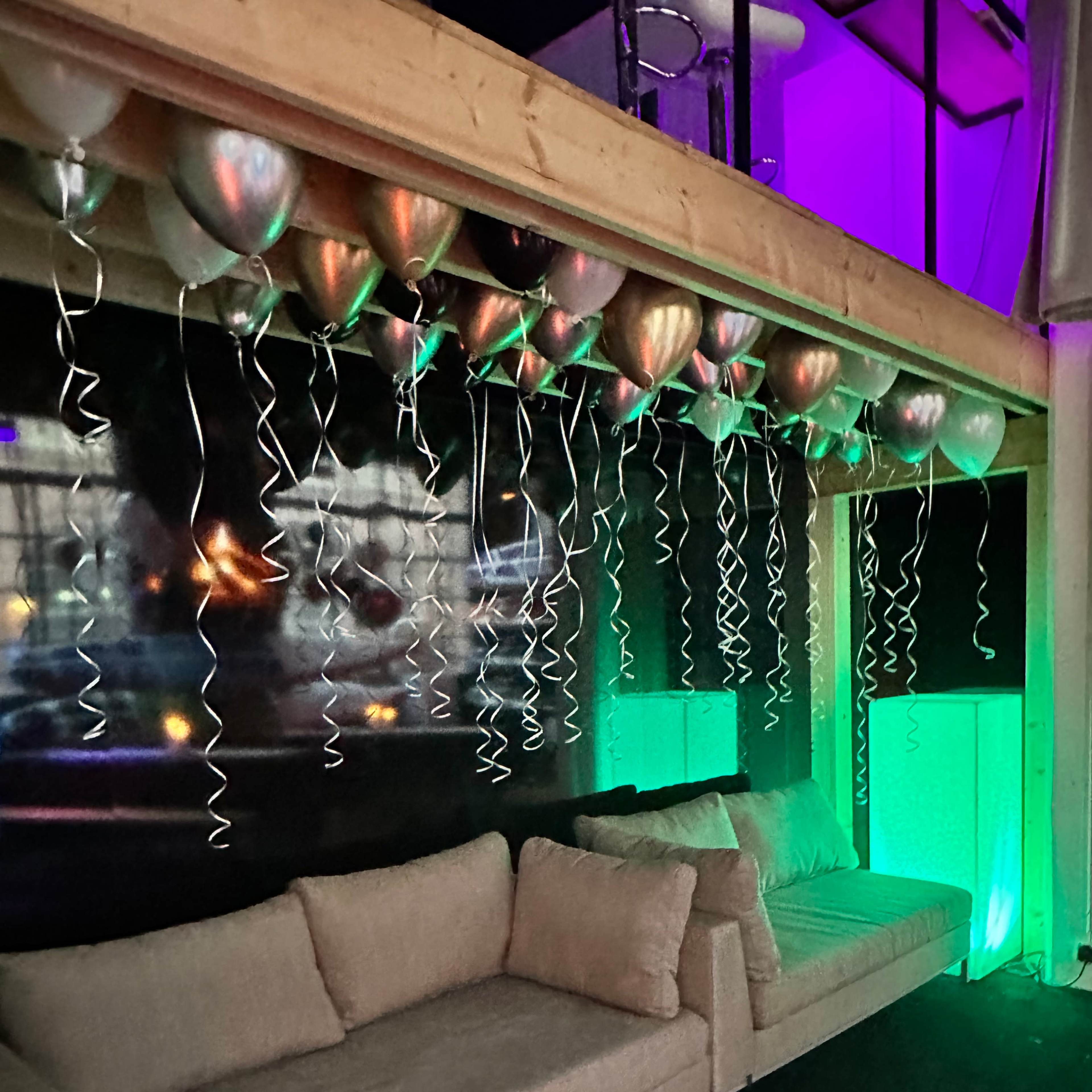 A cozy seating area features two light-colored sofas beneath a display of colorful balloons and streamers.