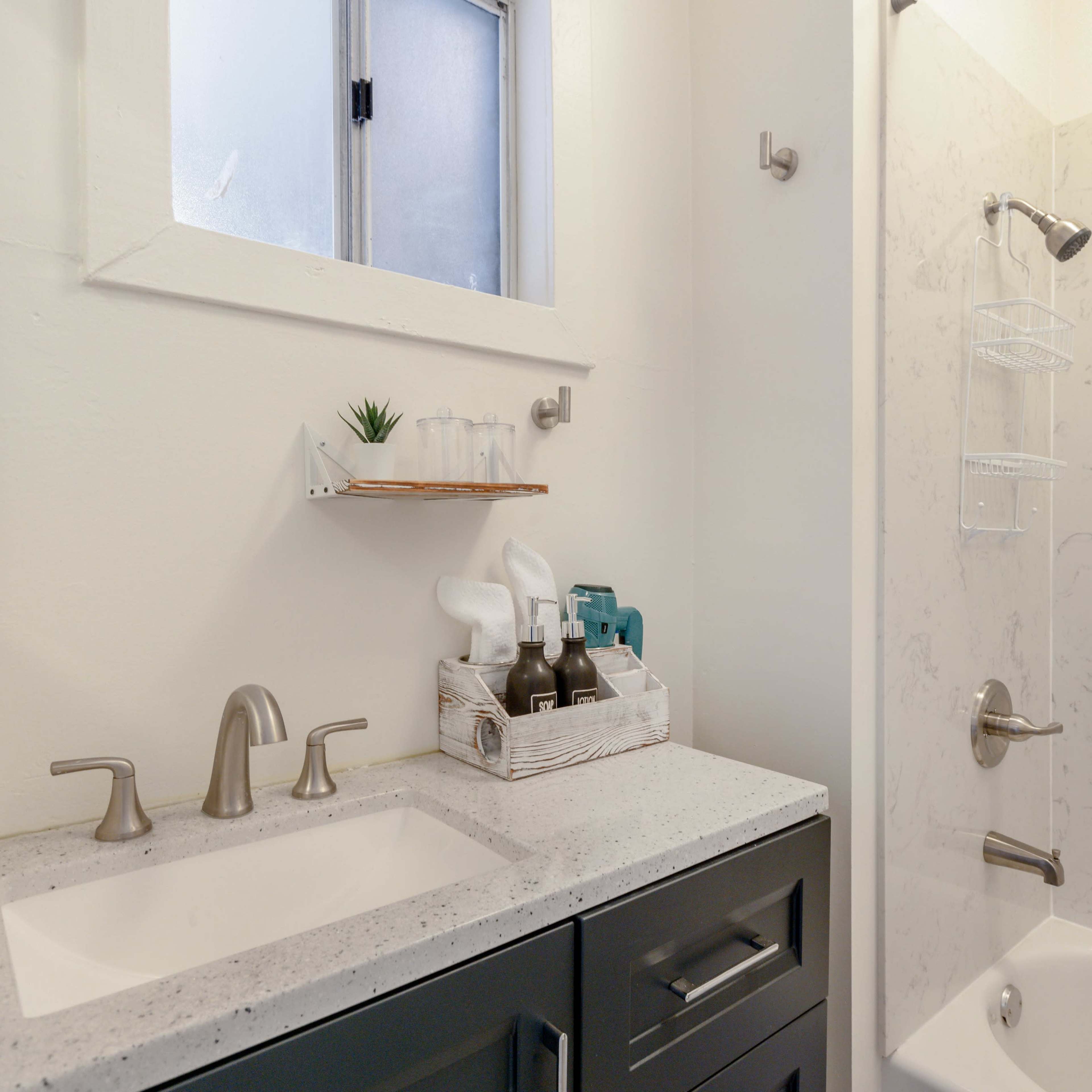 A modern bathroom with a white shower stall, a sink with gray cabinets, and a shelf holding toiletries.