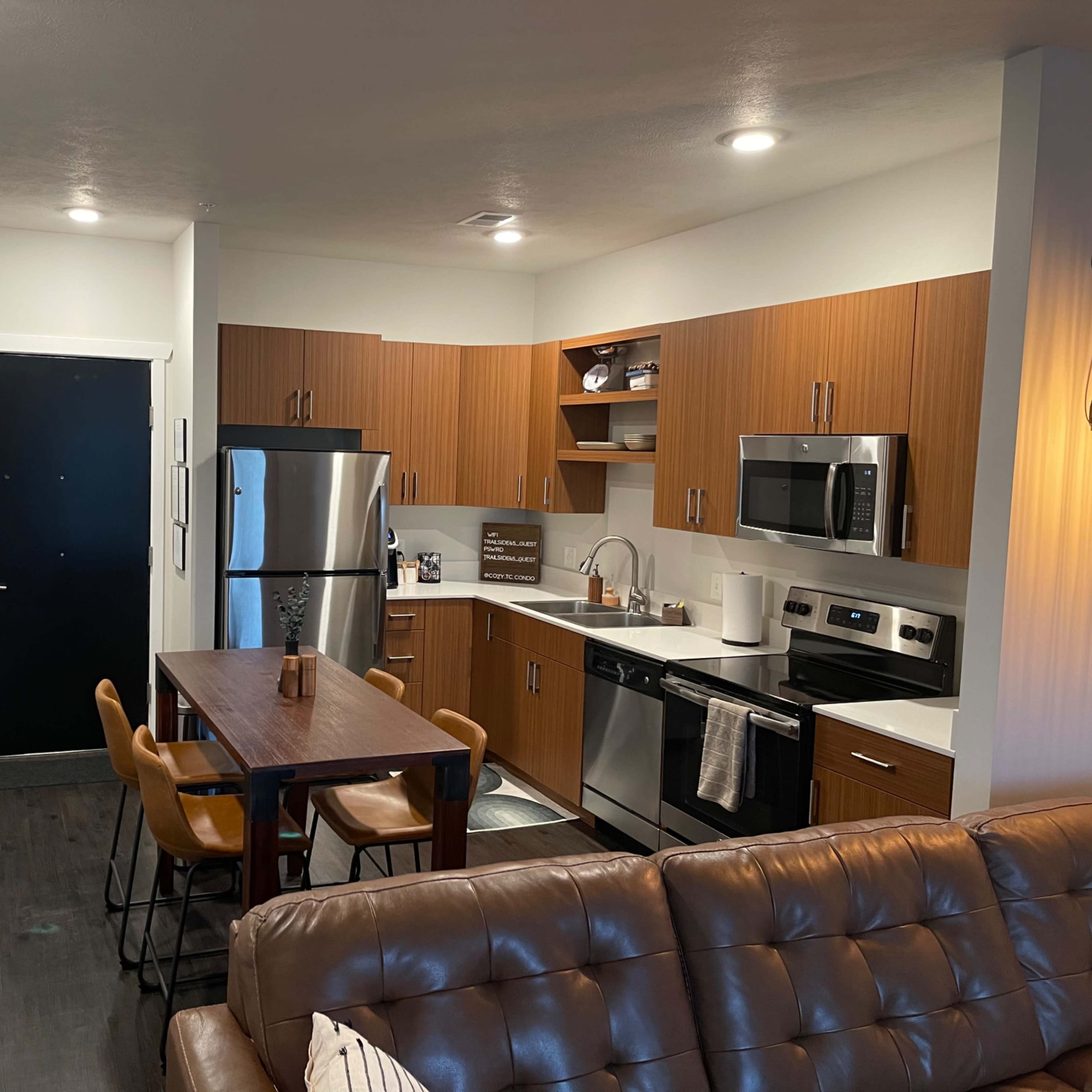 A modern kitchen and dining area with stainless steel appliances, wooden cabinets, and a table with four chairs.