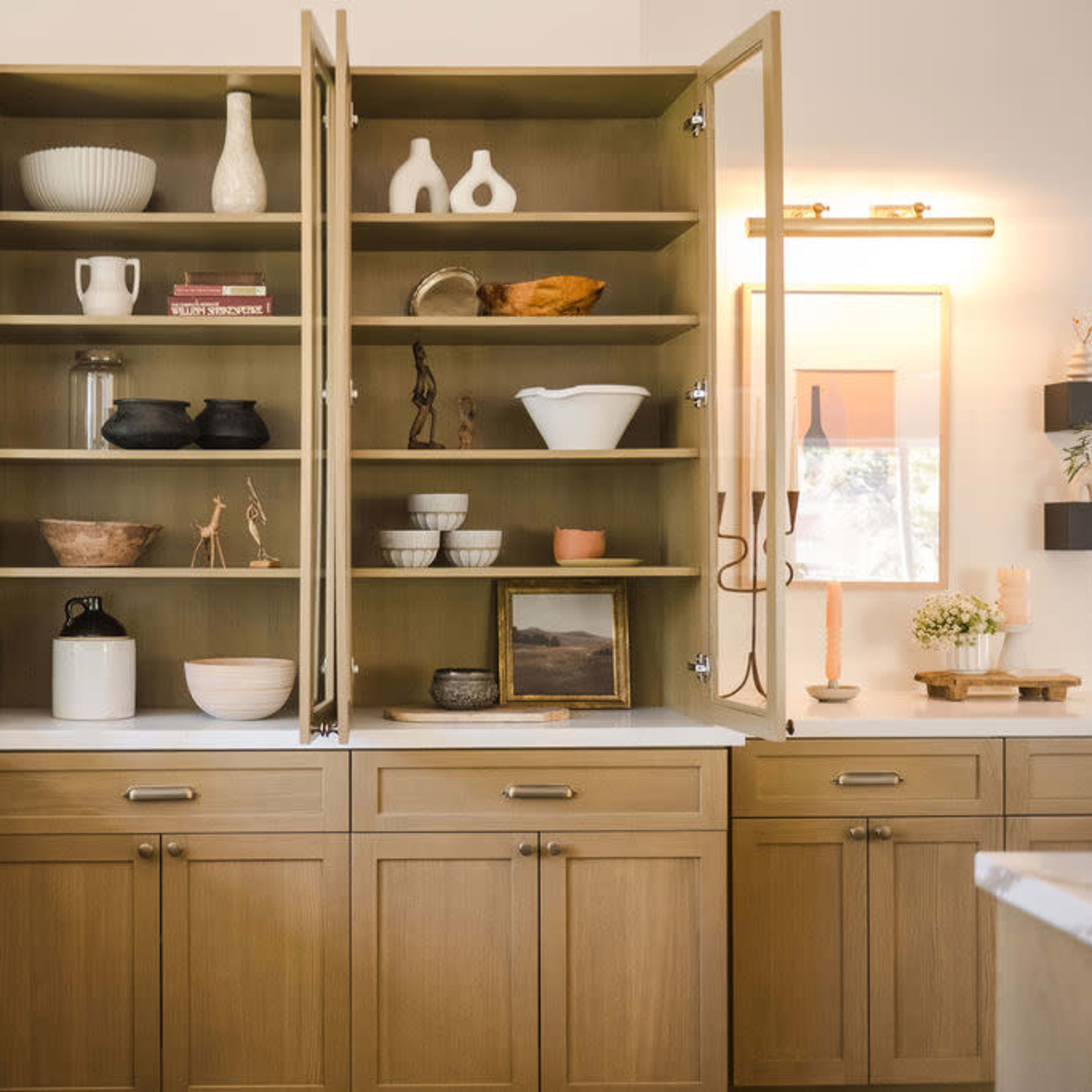 A well-organized kitchen cabinet with open shelves displaying various decorative items and dishware in a modern design.