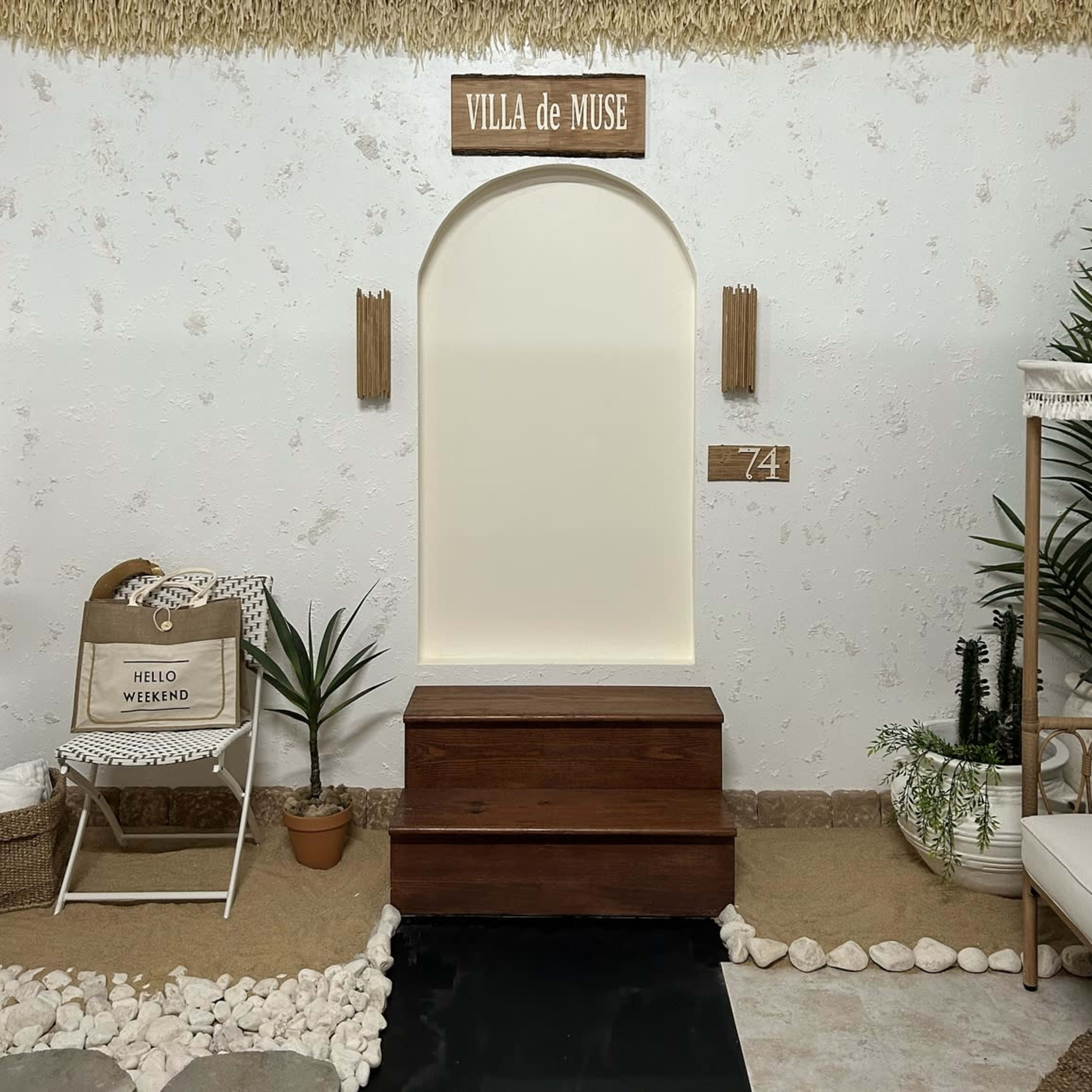 A minimalist interior space featuring a wooden chest, a decorative arch, and elements such as a plant, a chair, and a sign reading "VILLA de MUSE."