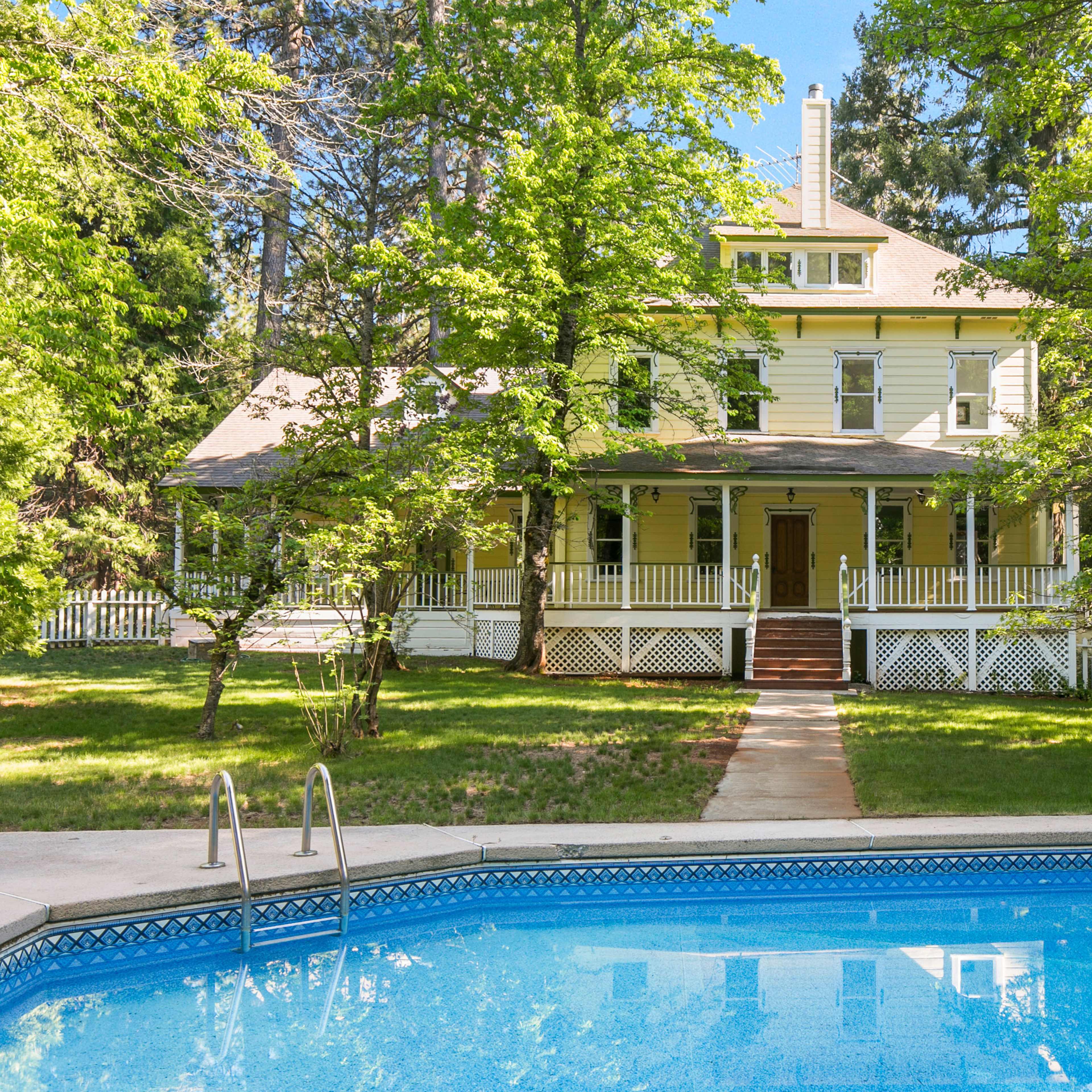 A large, two-story yellow house with a porch and surrounded by trees is visible behind a swimming pool.