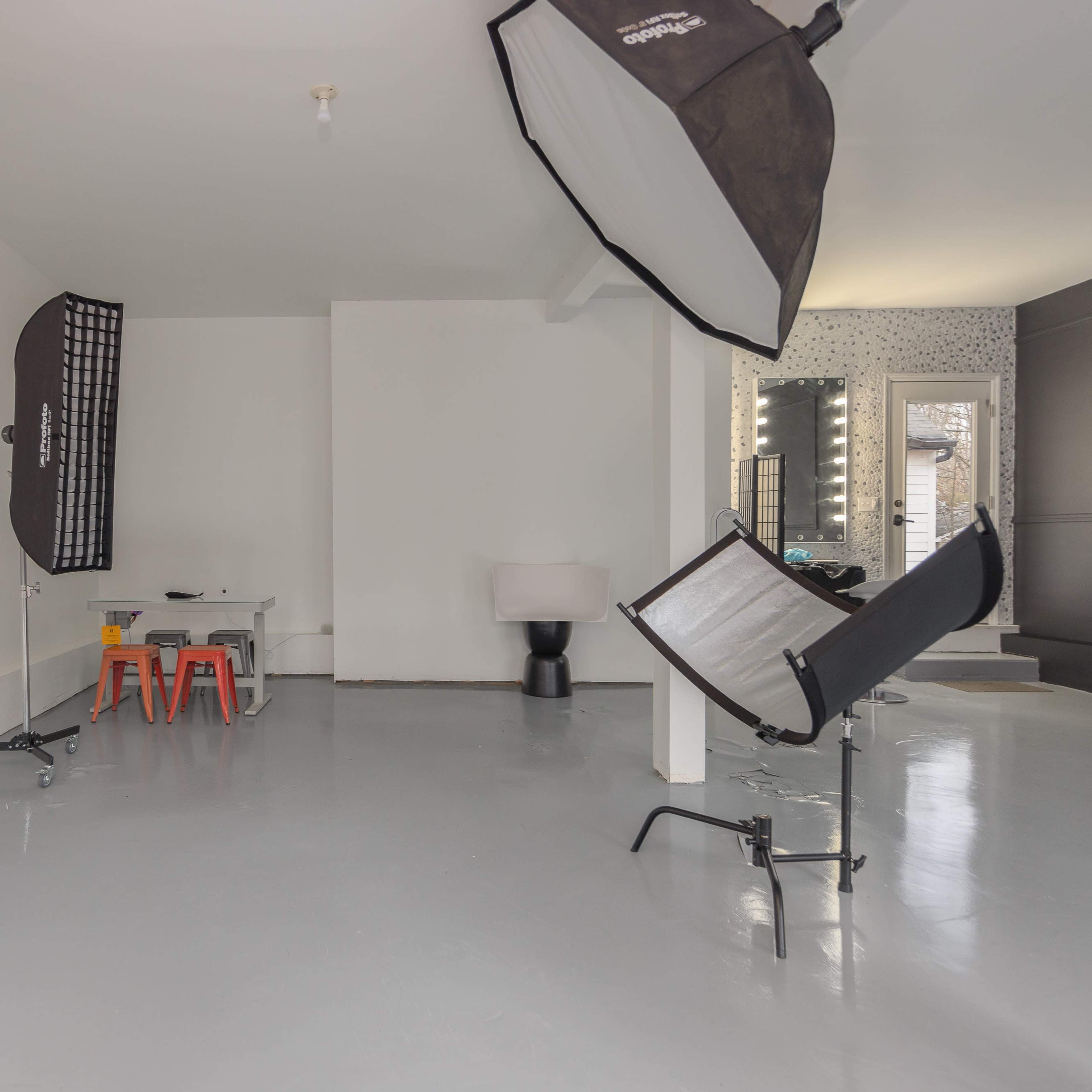 A minimal studio space equipped with photography lighting setups, a small table with chairs, and a lamp in the corner.