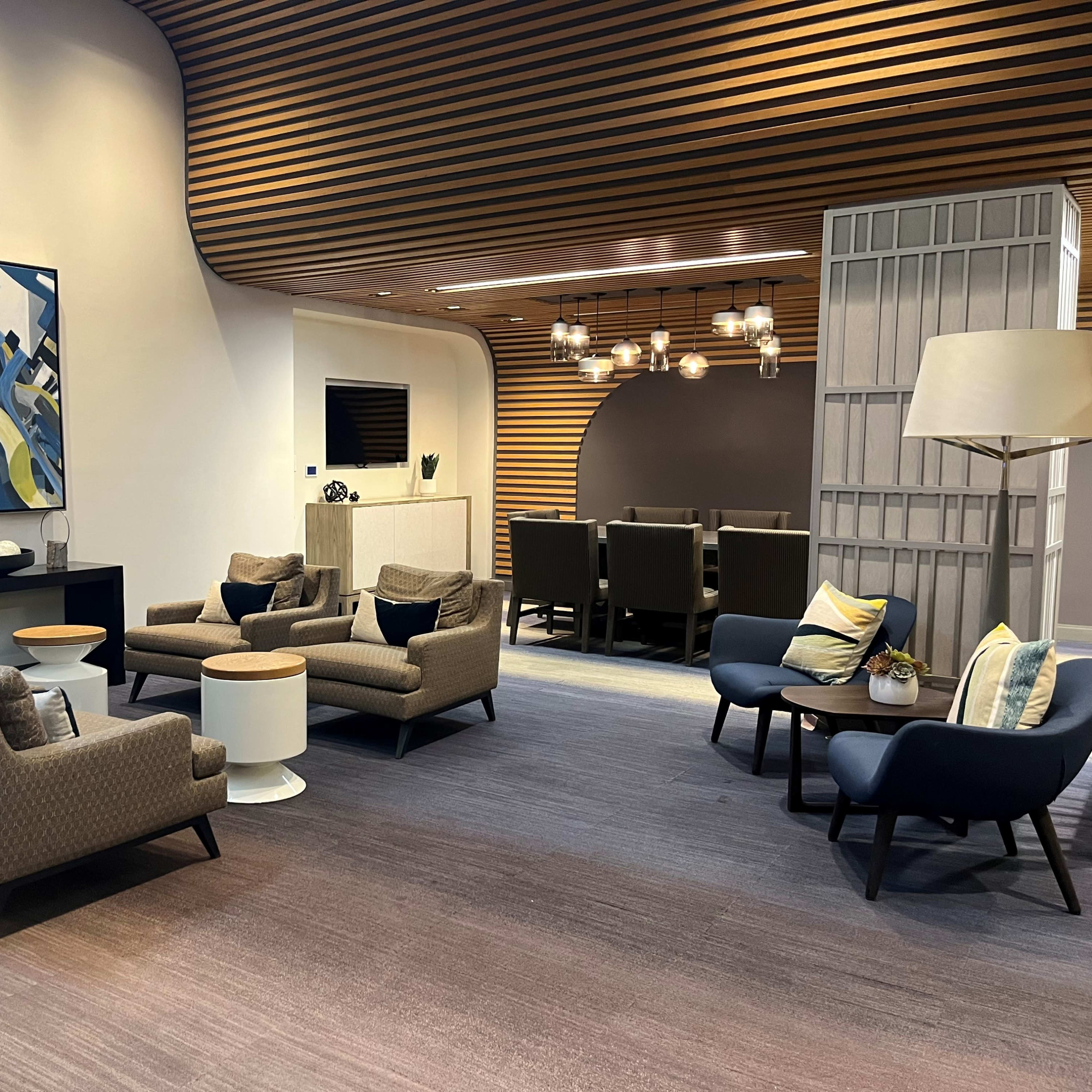 A modern lobby area with several patterned armchairs, a couple of small tables, and a large artwork on the wall, featuring a mix of colors.