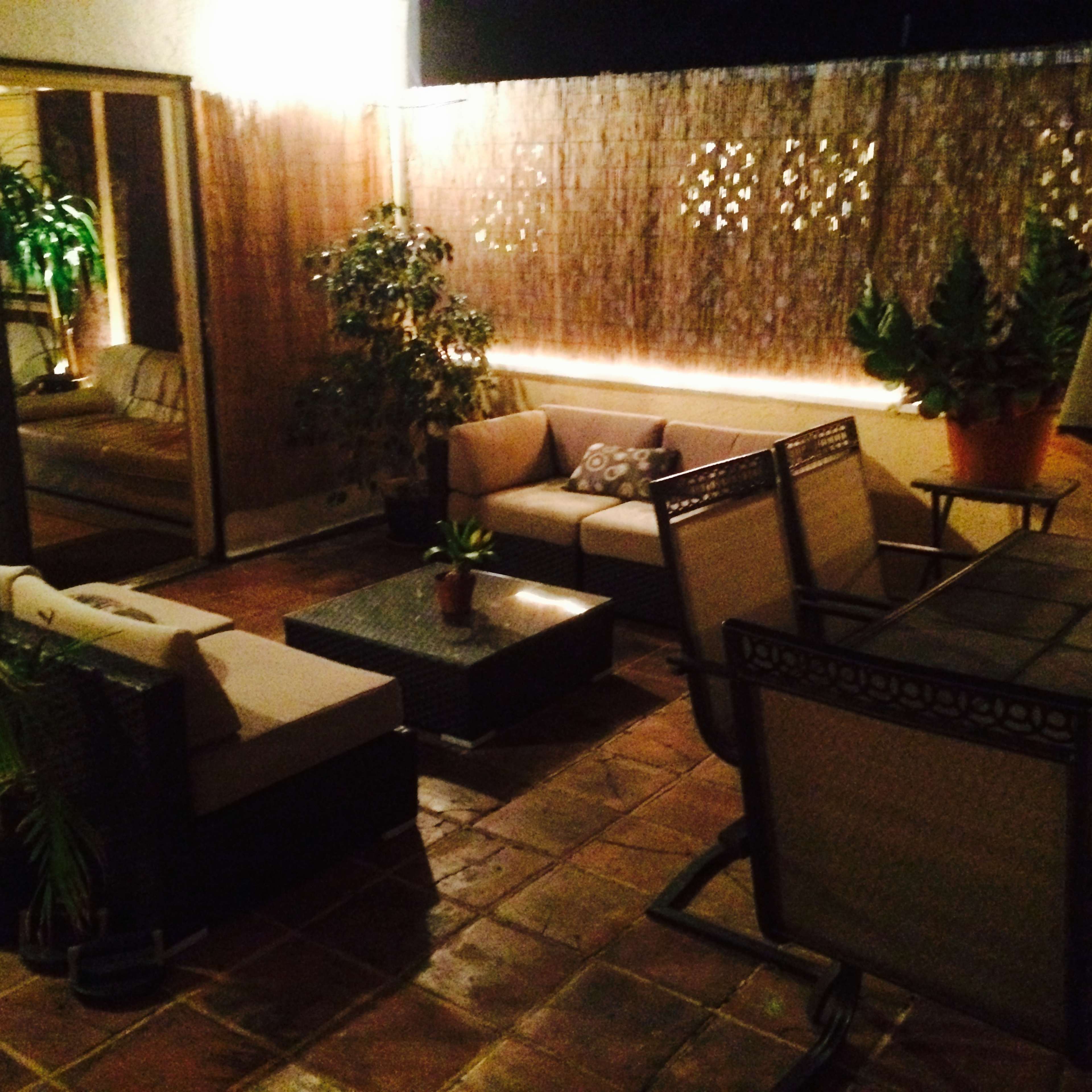 A cozy outdoor patio features a seating area with two sofas and a coffee table, surrounded by potted plants and illuminated by soft lighting.