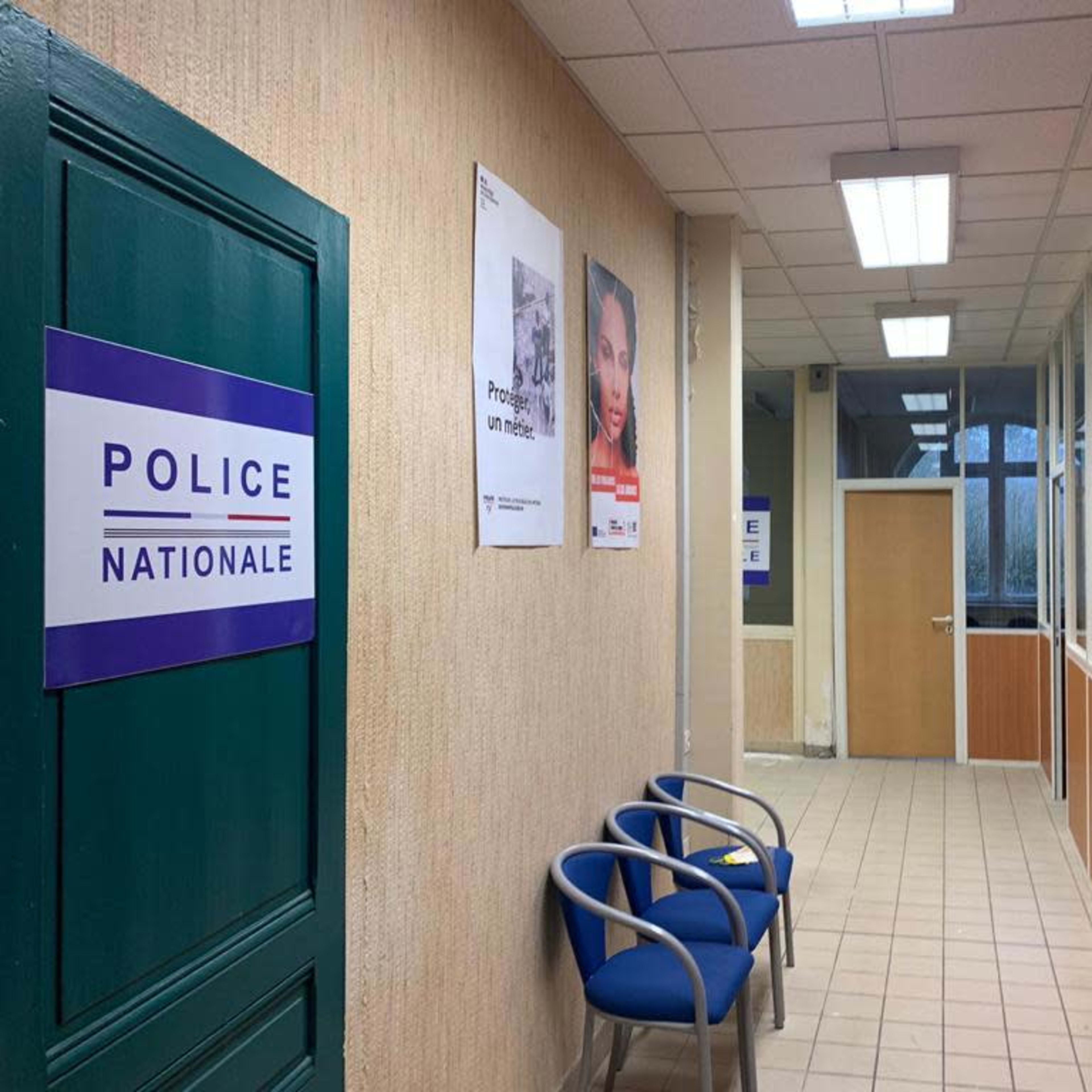 A hallway in a police station with blue chairs, signs for "Police Nationale," and posters on the walls.