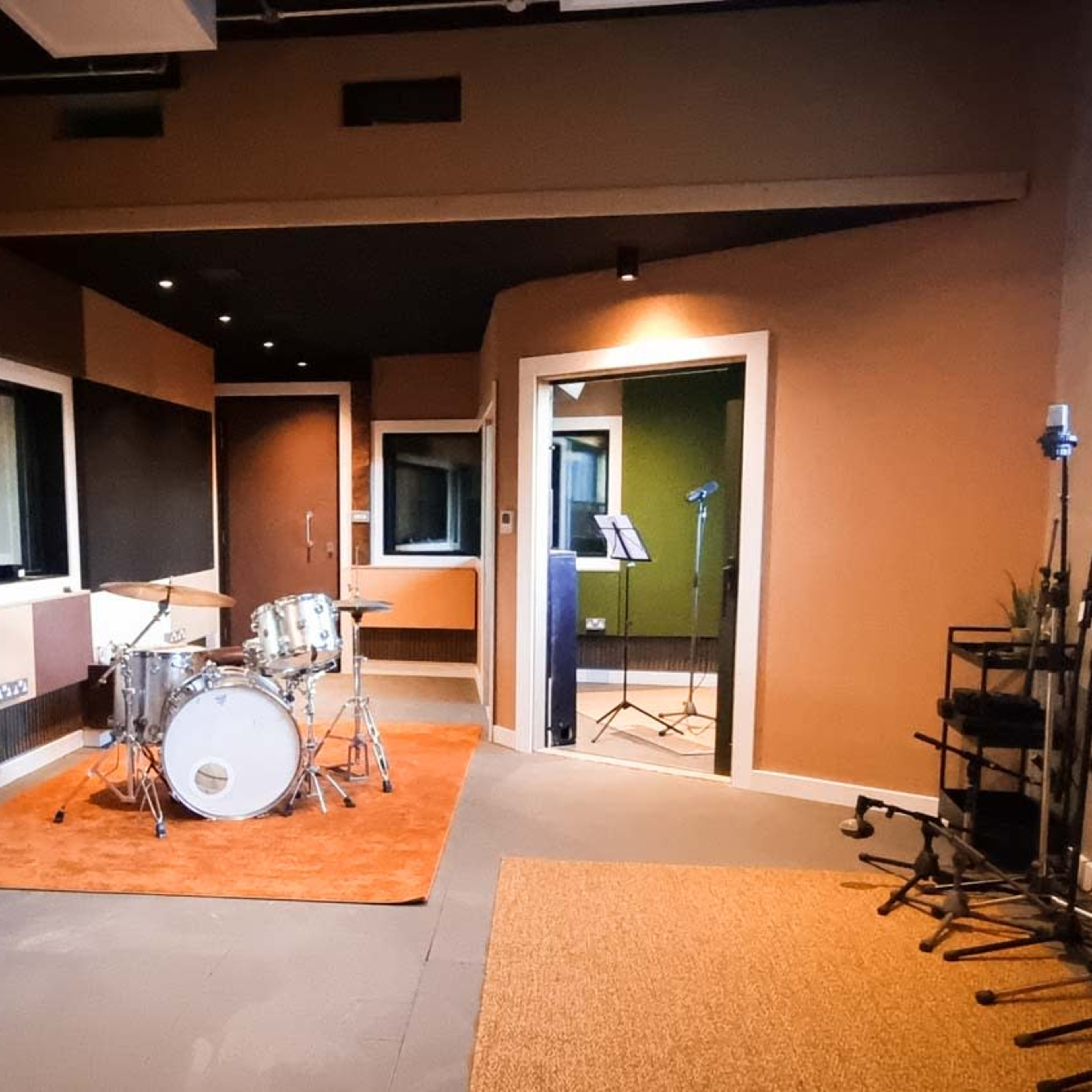 A soundproof recording studio with a drum set in one corner, various microphones positioned around the room, and a glass window separating different sections.