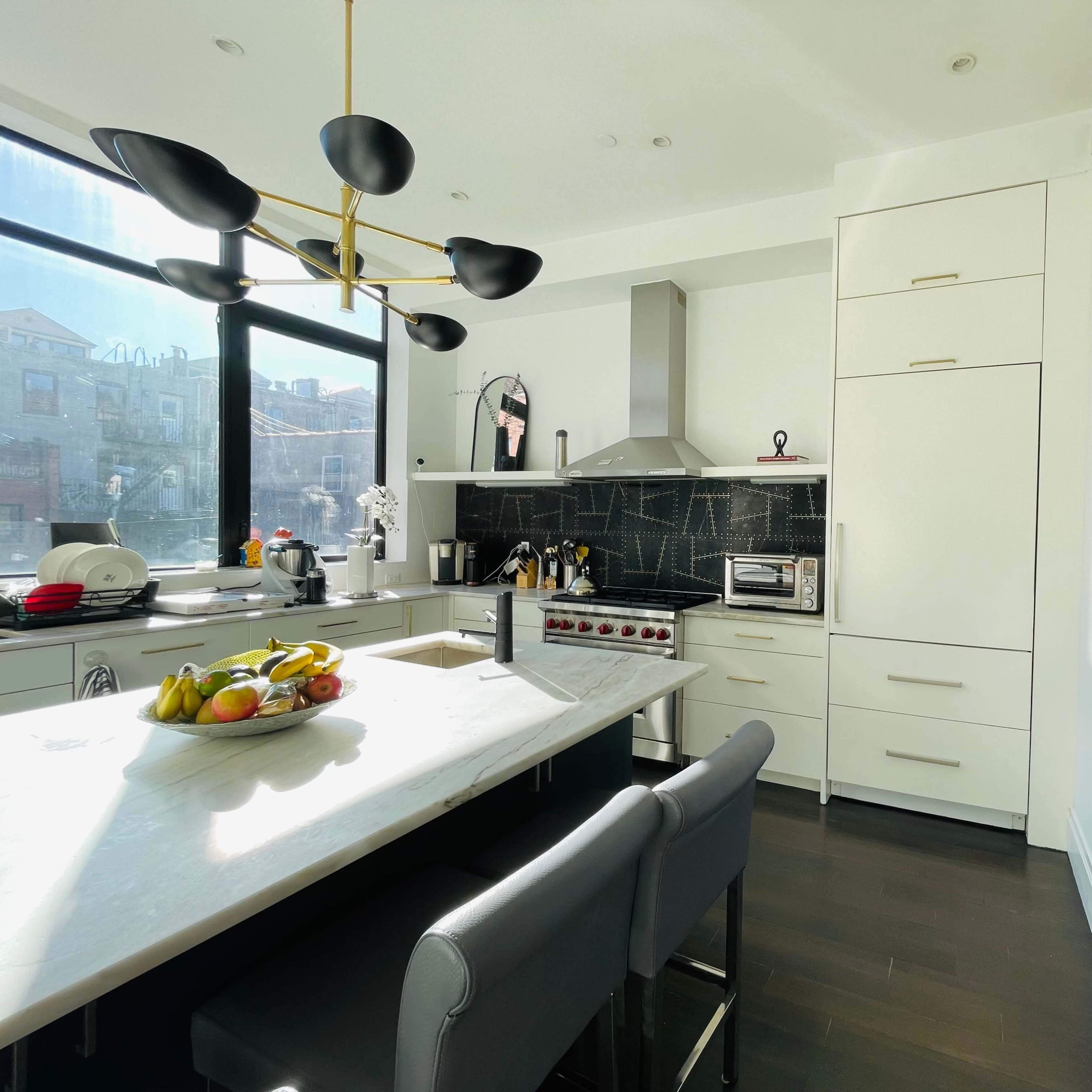 A modern kitchen featuring a central island with a fruit bowl, a sleek stove, and white cabinetry against a black tiled backsplash.