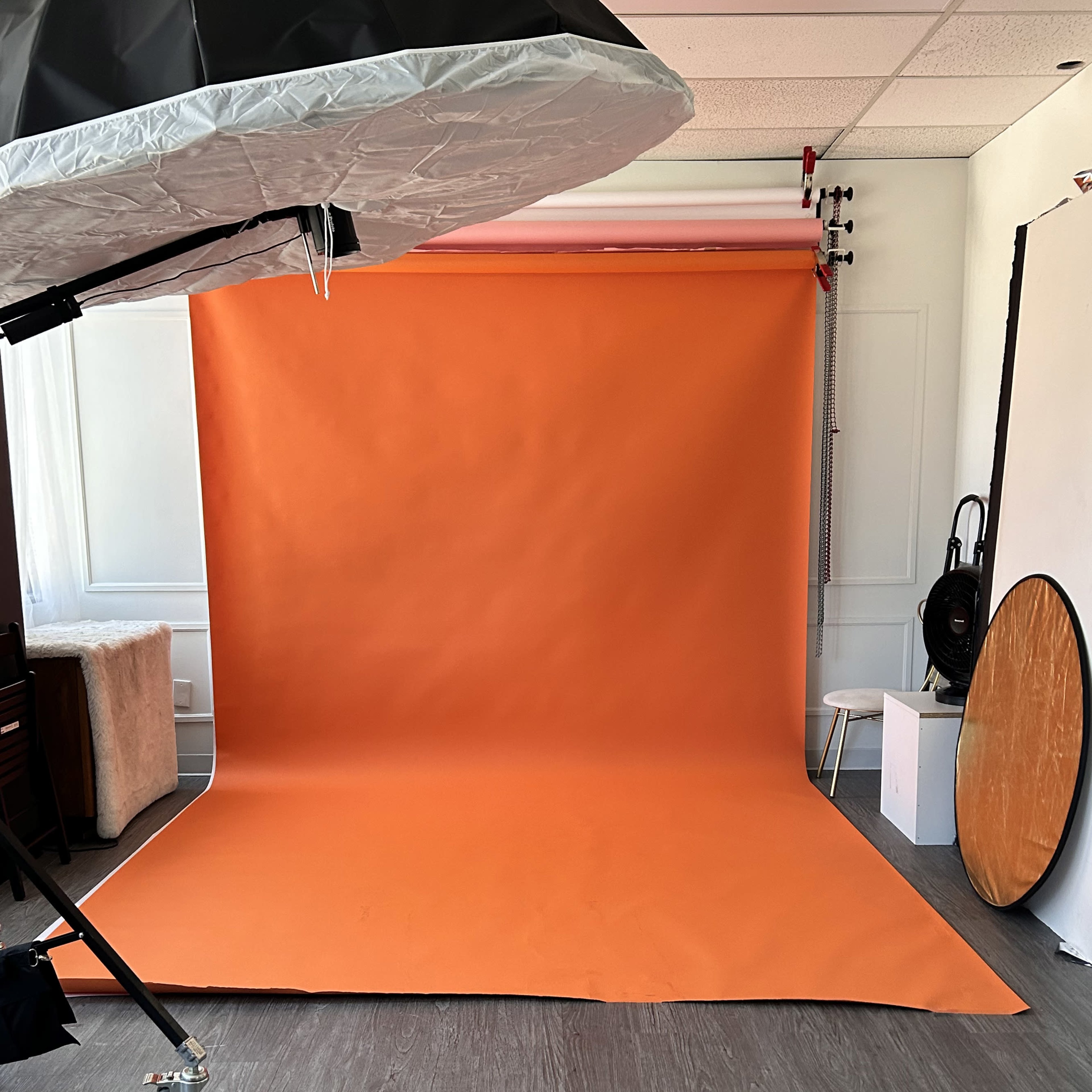 A photography studio with an orange backdrop, a lighting umbrella, and a circular mirror on the floor.